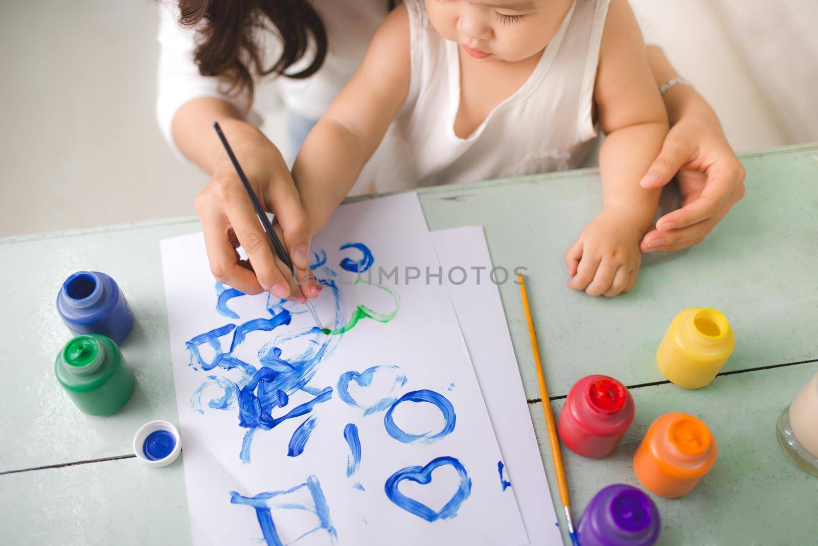 Happy family mother and daughter together paint. Asian woman helps her child girl.