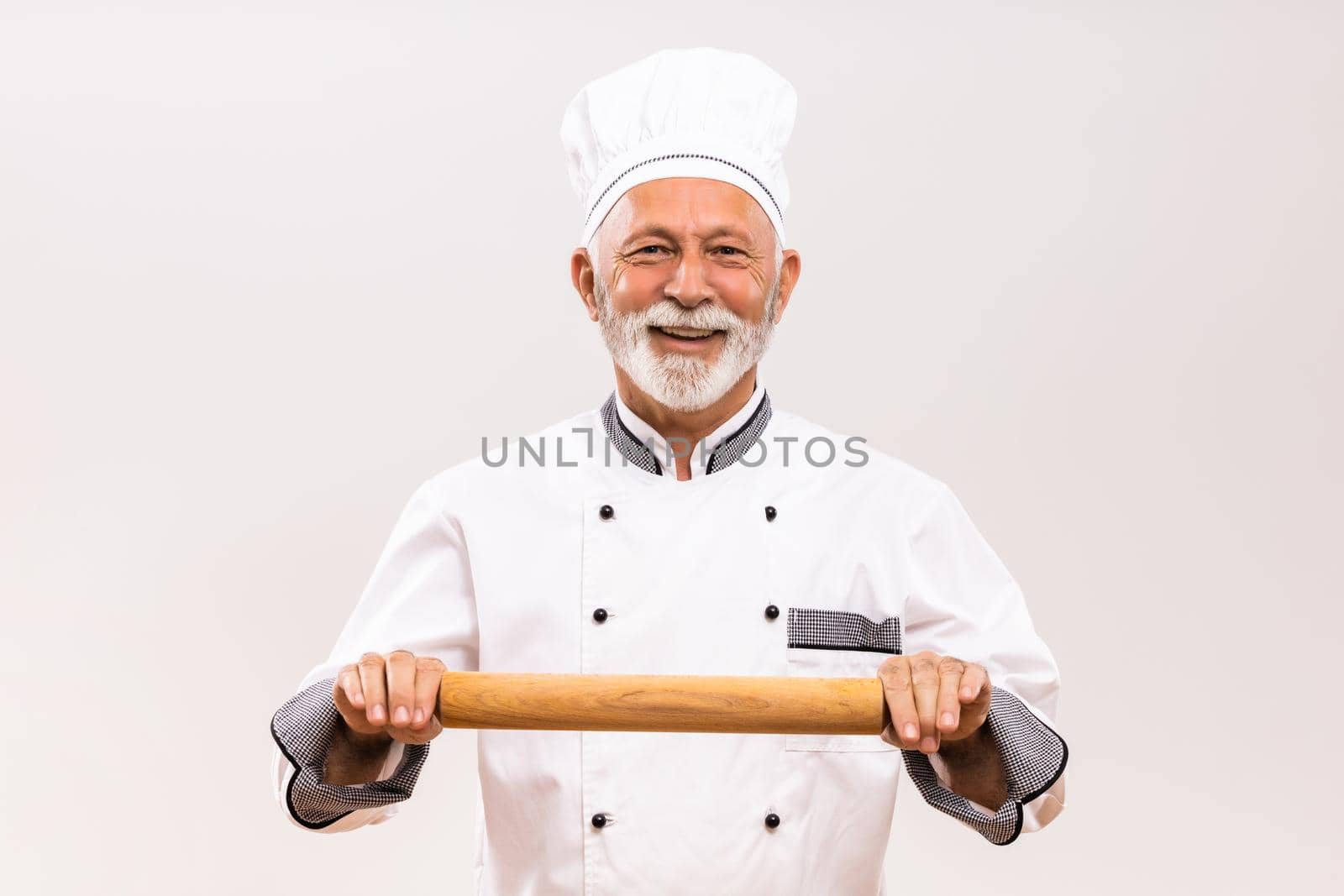 Portrait of senior chef holding rolling pin on gray background.
