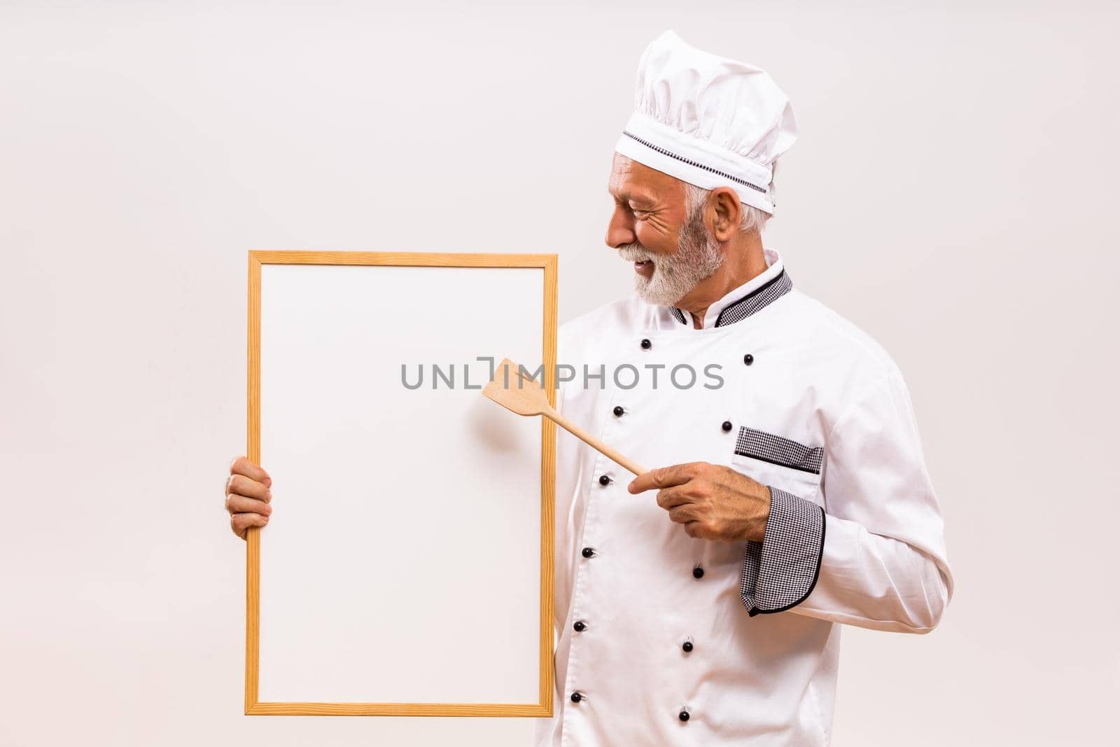 Portrait of senior chef showing with wooden spoon whiteboard by Bazdar