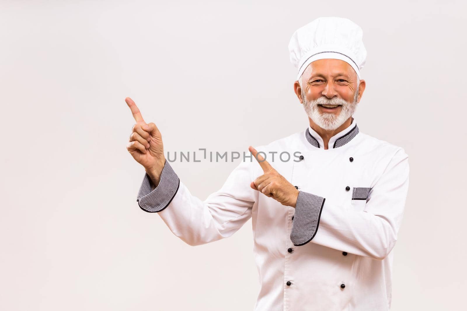 Portrait of  senior chef  pointing on gray background.