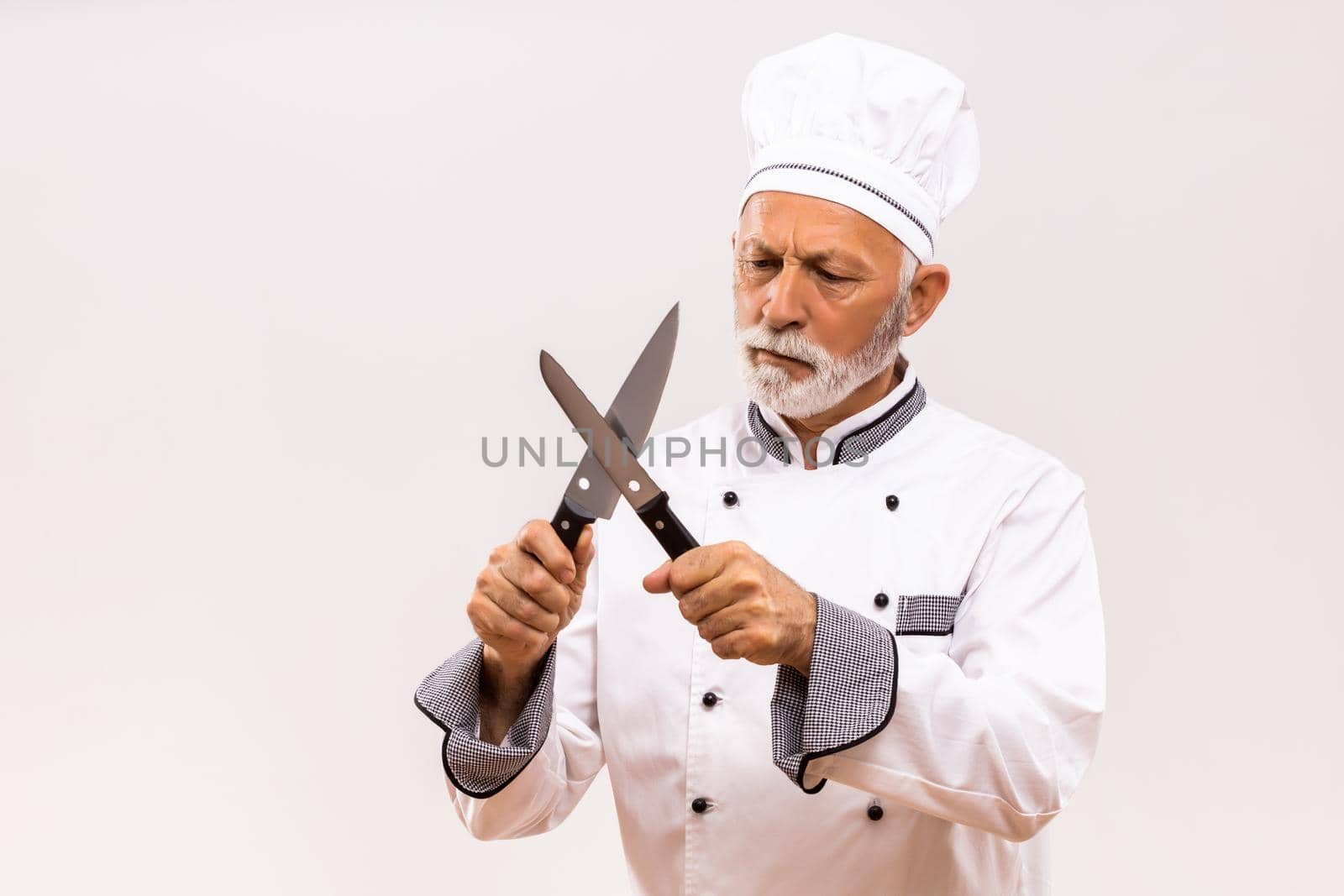 Image of angry chef sharpens knives on gray background.