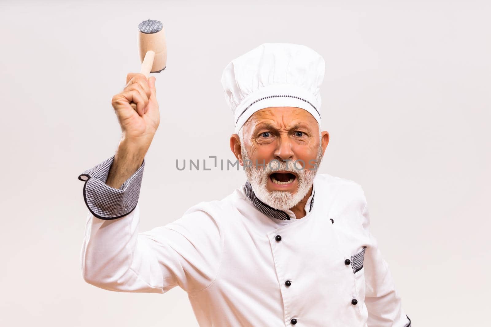 Image of angry senior chef holding work tool and shouting.