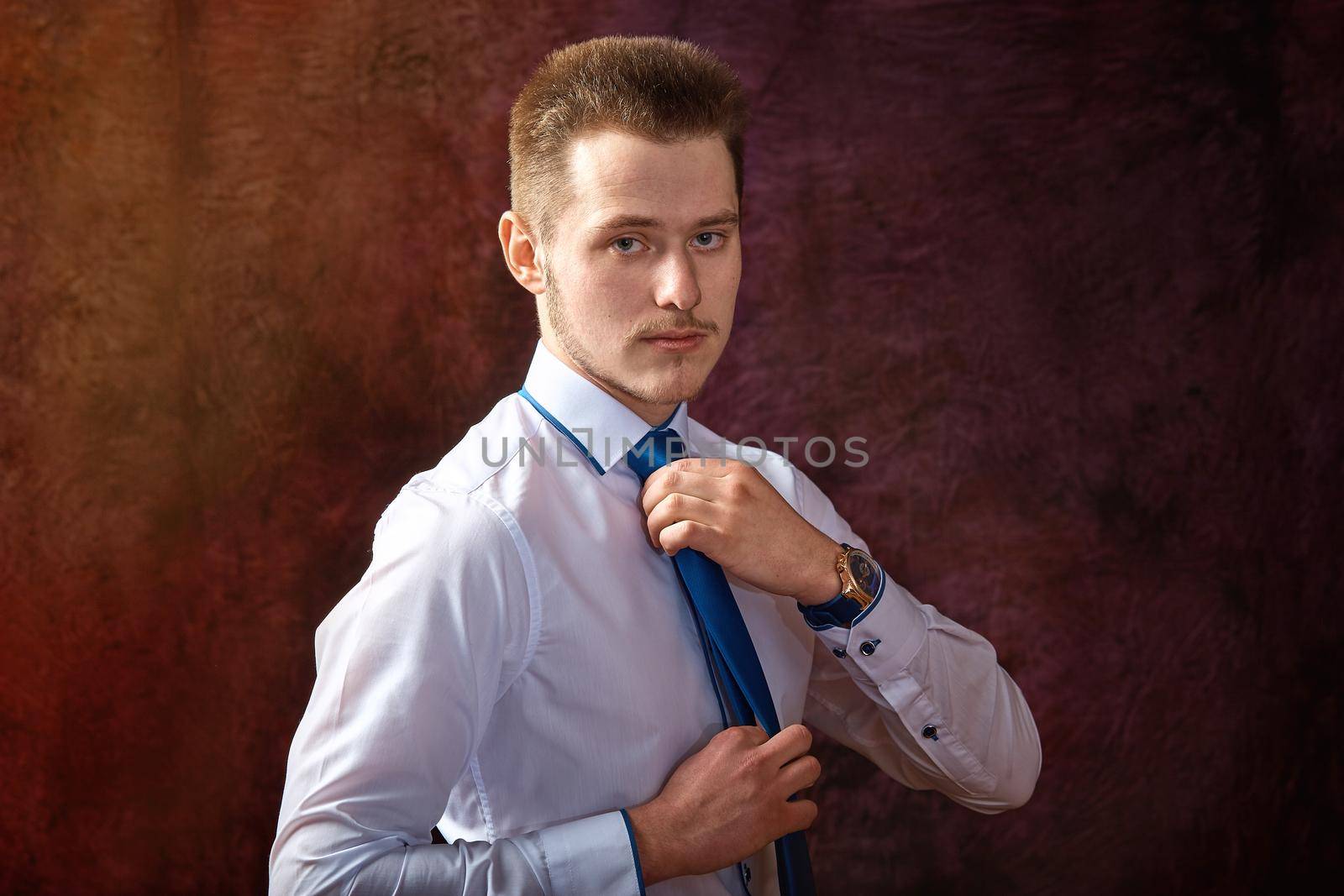 Handsome young man in a white shirt and tie on a gray background.Adjusts the tie
