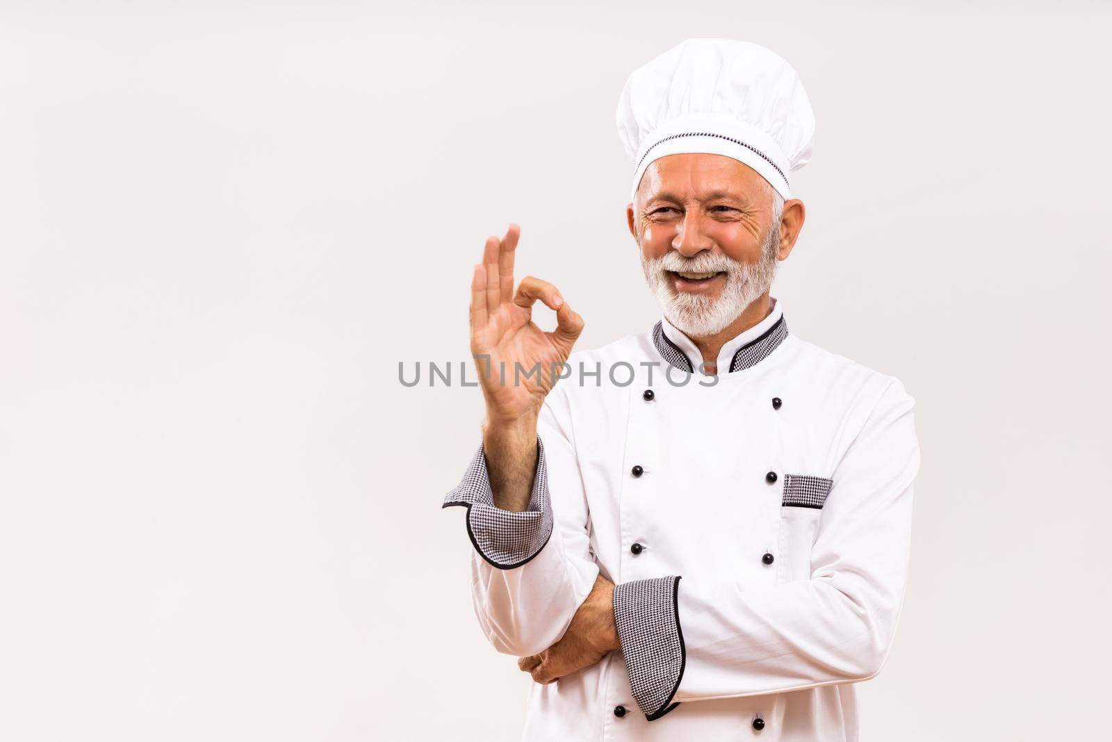 Portrait of senior chef showing ok sign on gray background.