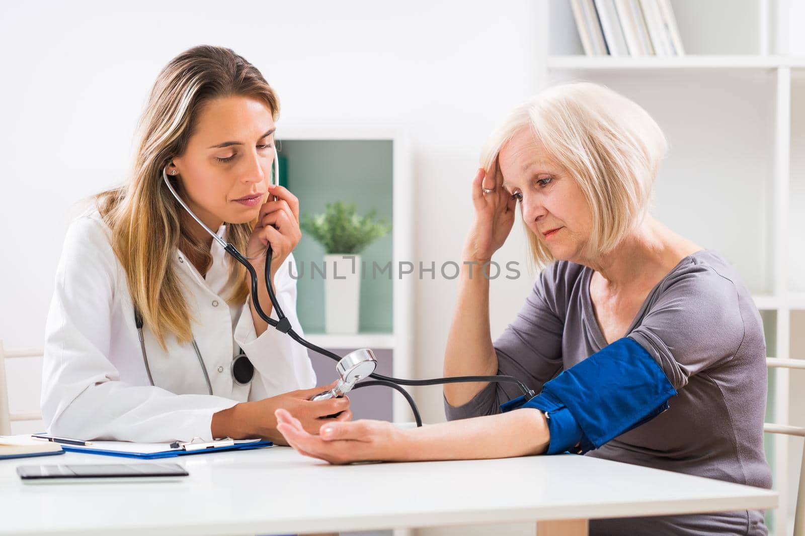 Female doctor is measuring blood pressure to her senior patient in doctor's office.