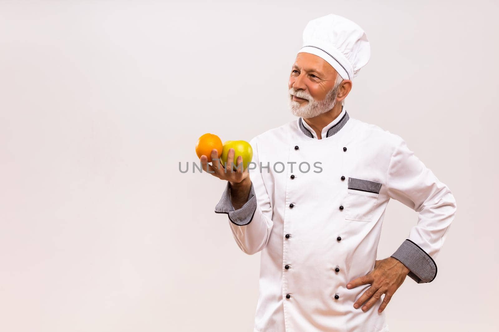 Image of senior chef holding  fruit and thinking on gray background.