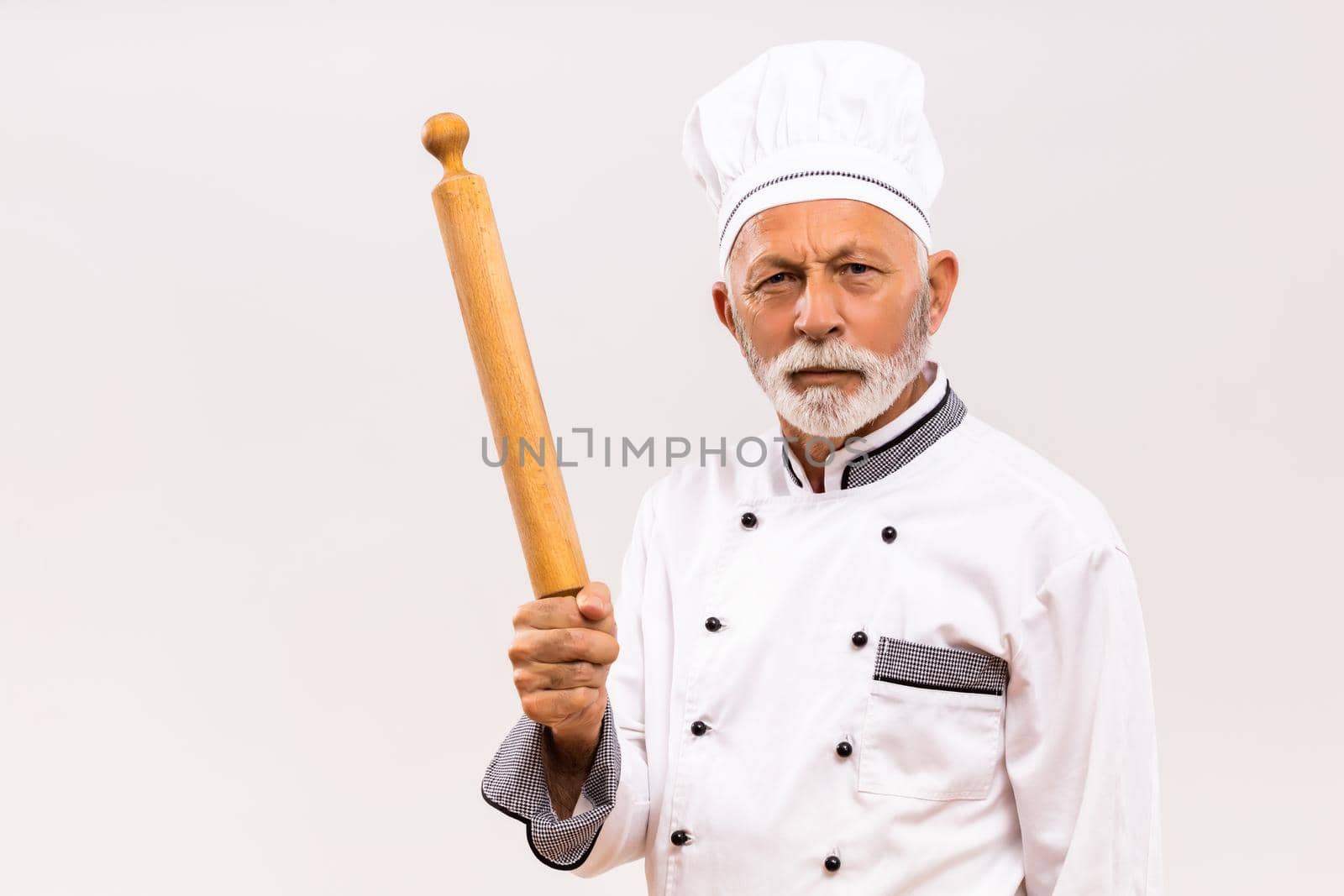 Image of angry senior chef holding rolling pin on gray background.