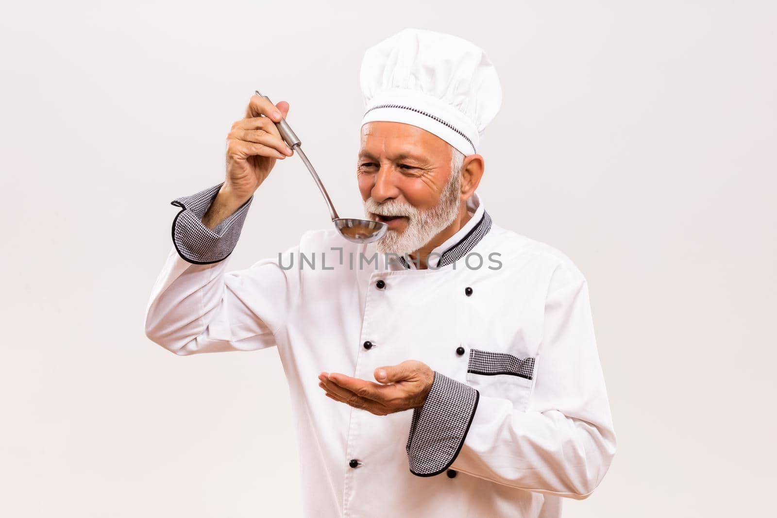 Portrait of content senior chef tasting soup.