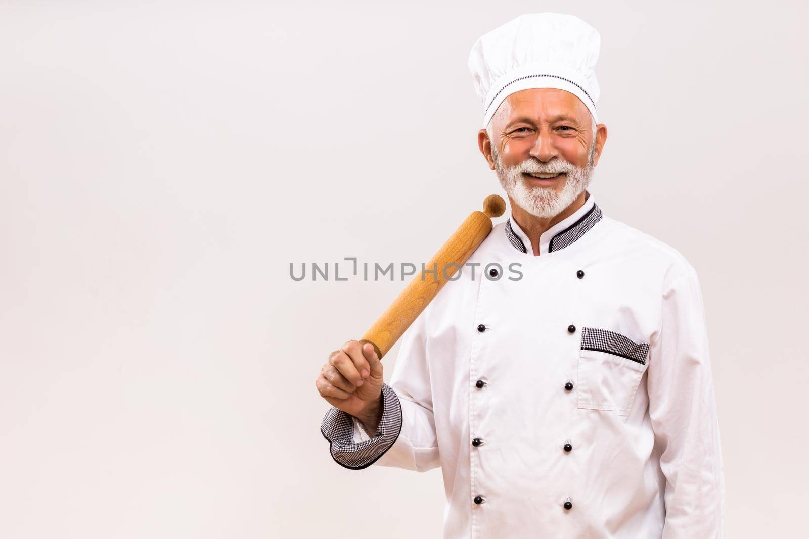 Portrait of senior chef with rolling pin on gray background.