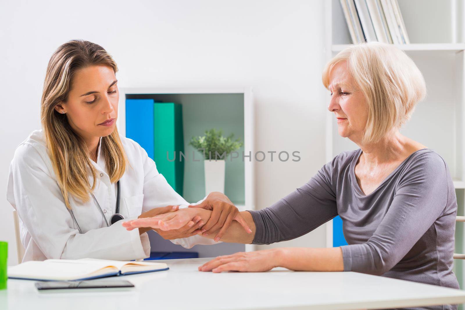 Female doctor examines her senior patient's wrist by Bazdar