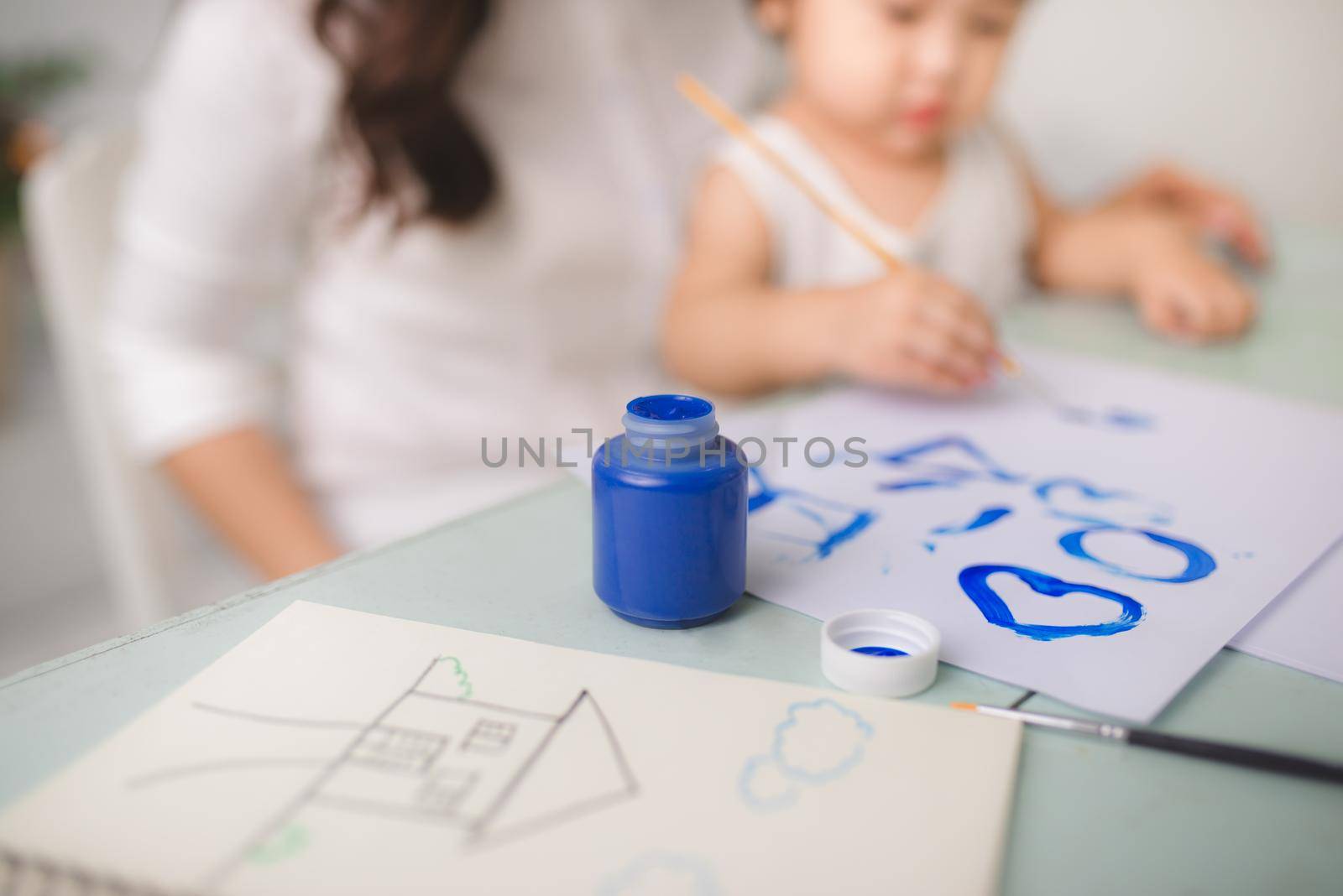 Happy family mother and daughter together paint. Asian woman helps her child girl.