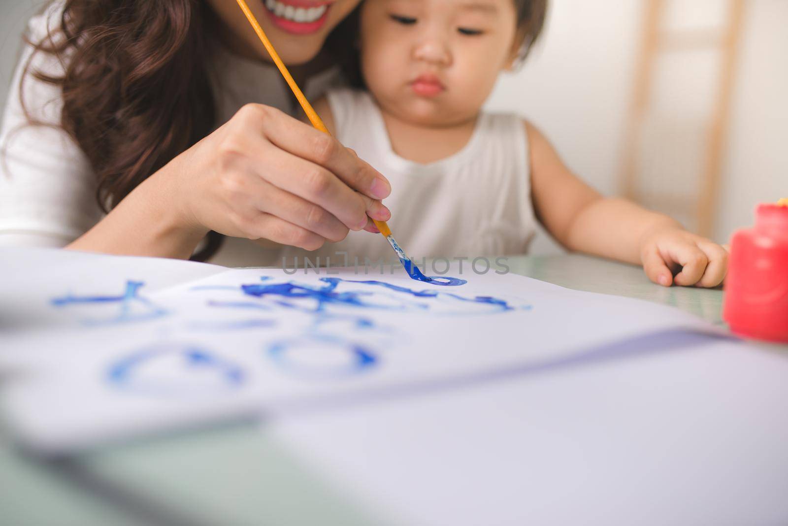 Happy family mother and daughter together paint. Asian woman helps her child girl.