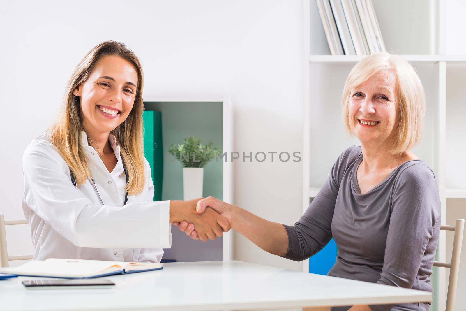 Female doctor and happy senior woman patient shaking hands by Bazdar