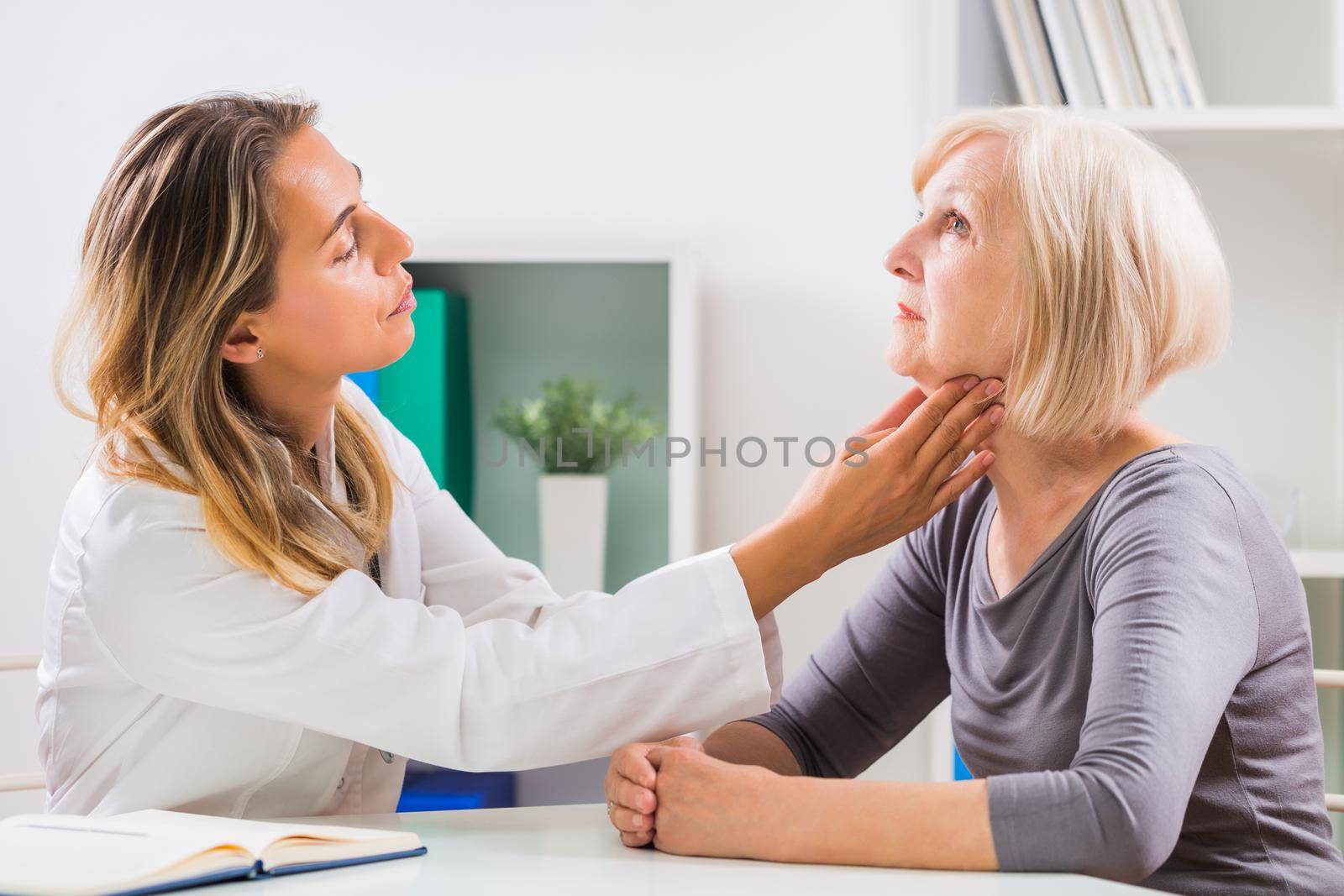 Female doctor examines her senior patient's throat in office.