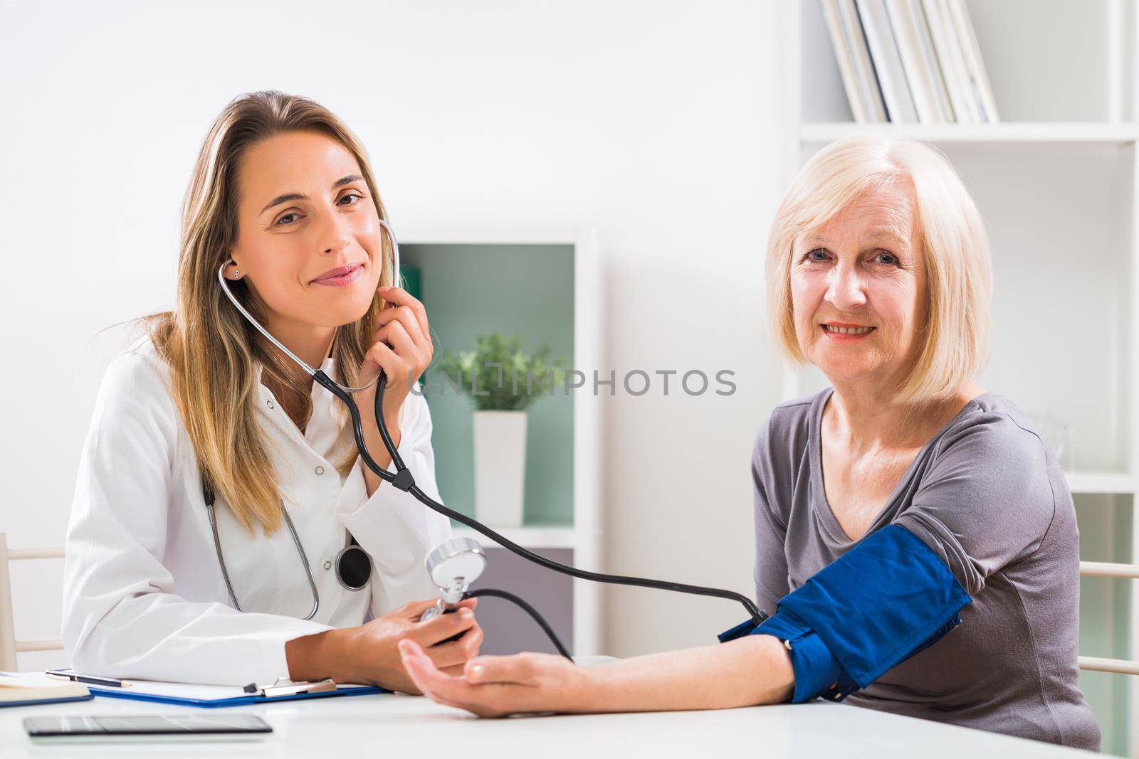 Female doctor is measuring blood pressure to her senior patient in doctor's office.