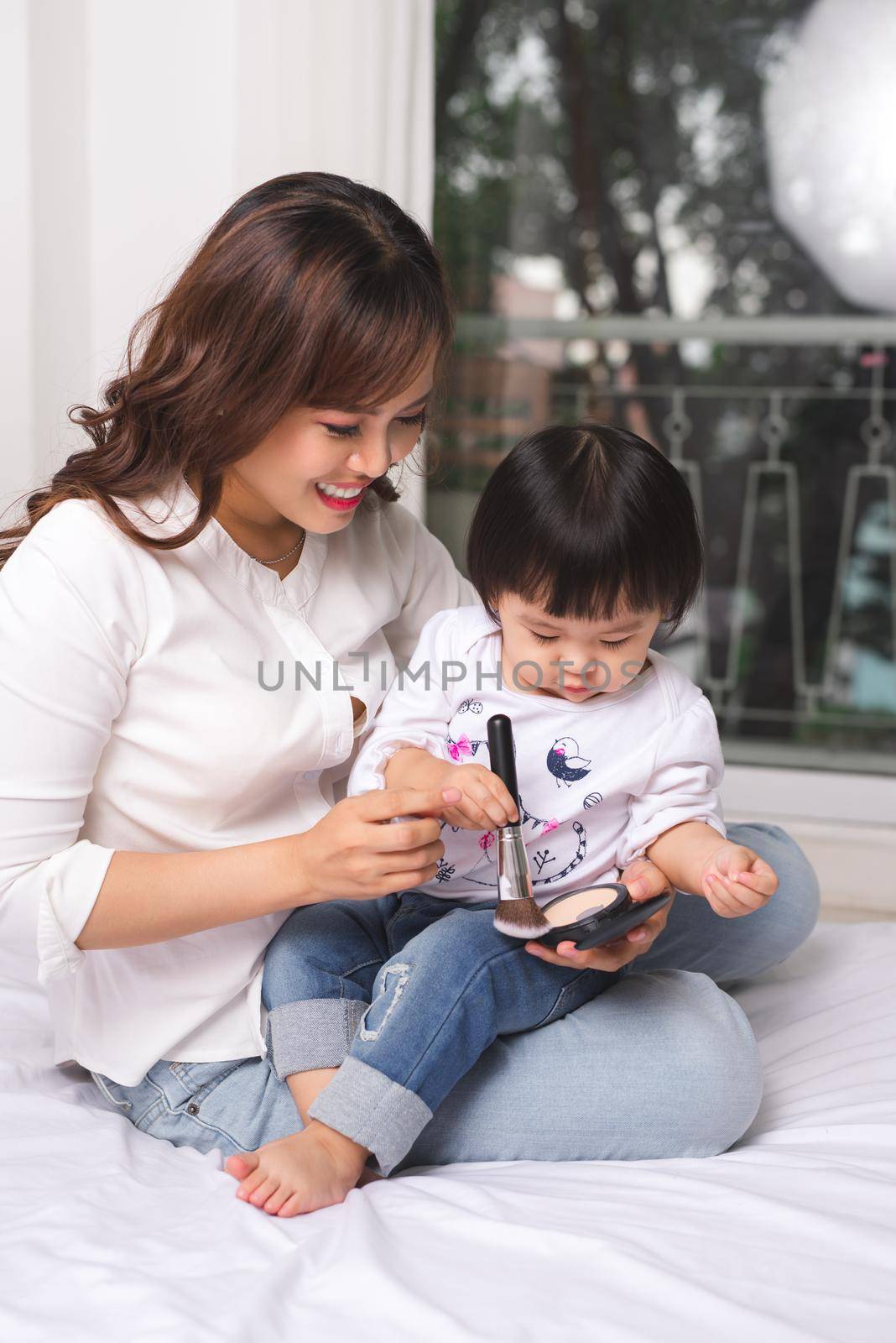 Lovely princess is applying the make up on her skin with special brush as she wants to look like her adult mother by makidotvn