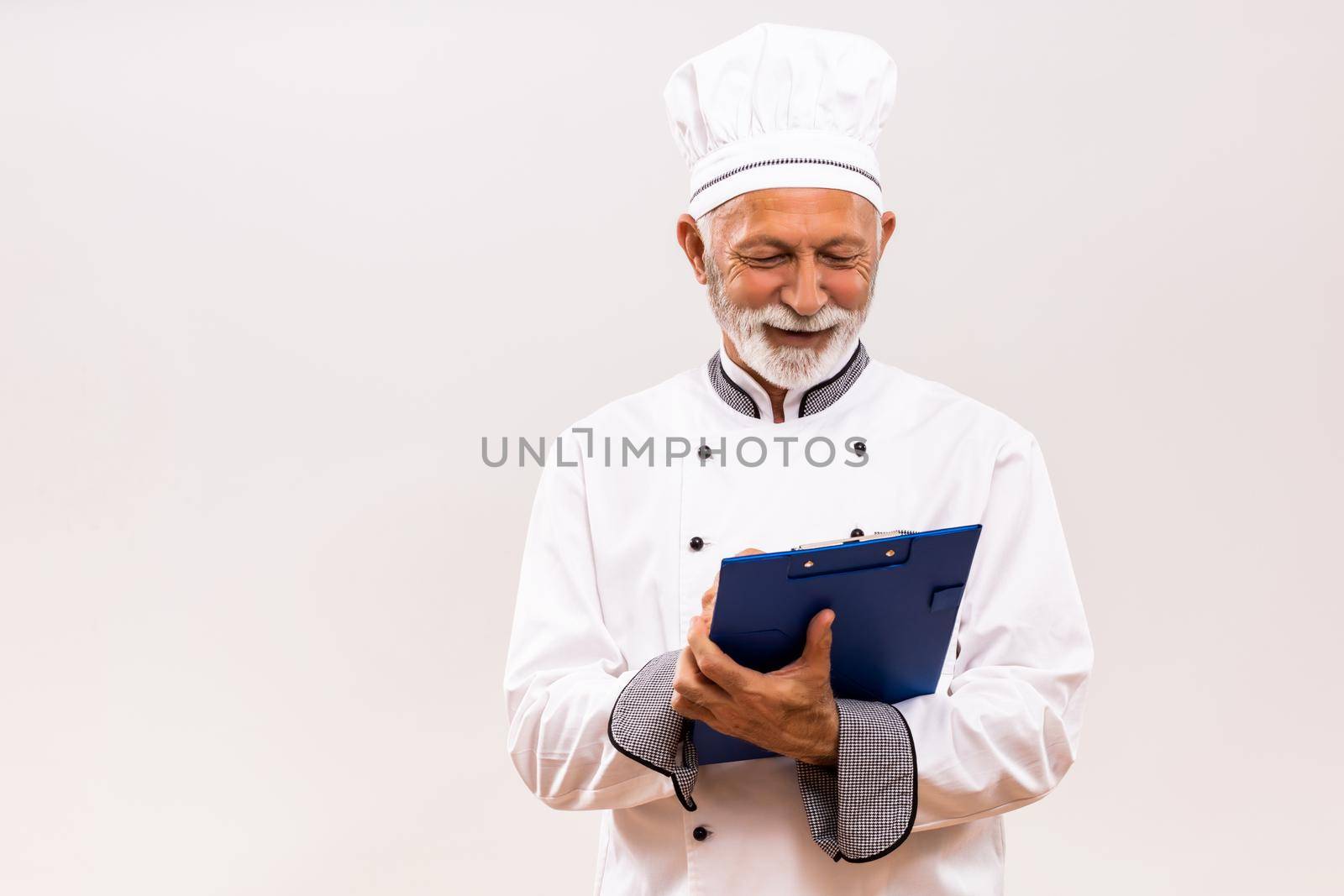 Portrait of senior  chef holding cookbook on gray background.