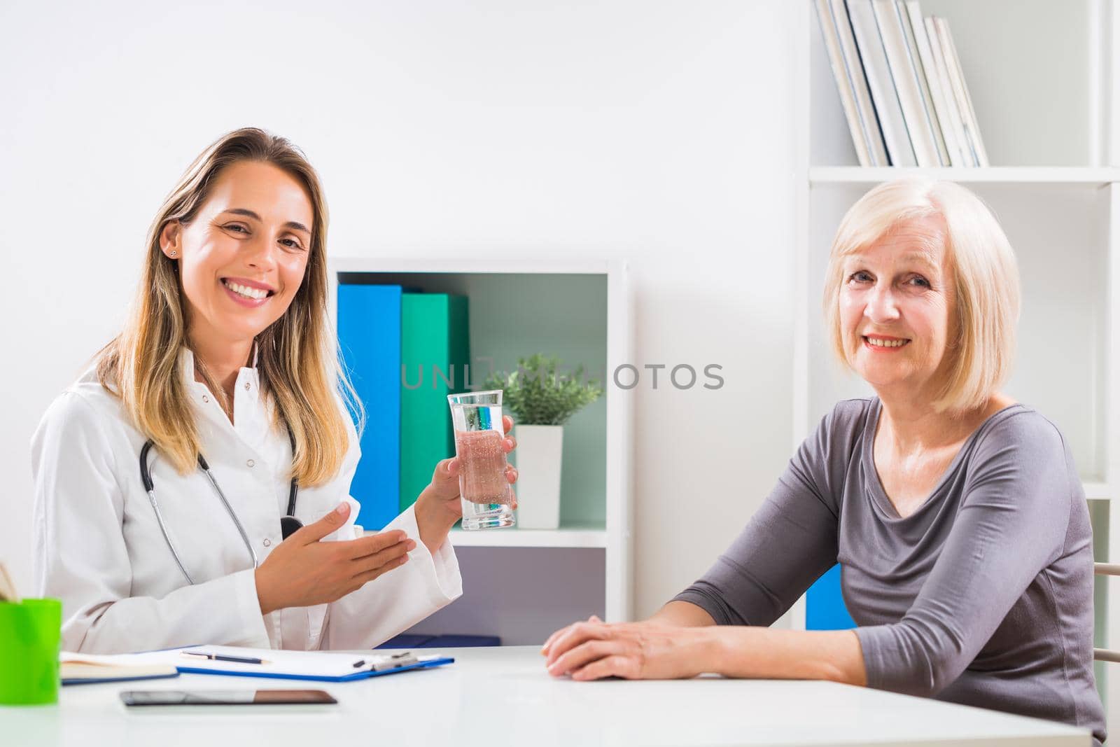 Female doctor is giving advice how is important to drink a lot of water to her senior woman patient .