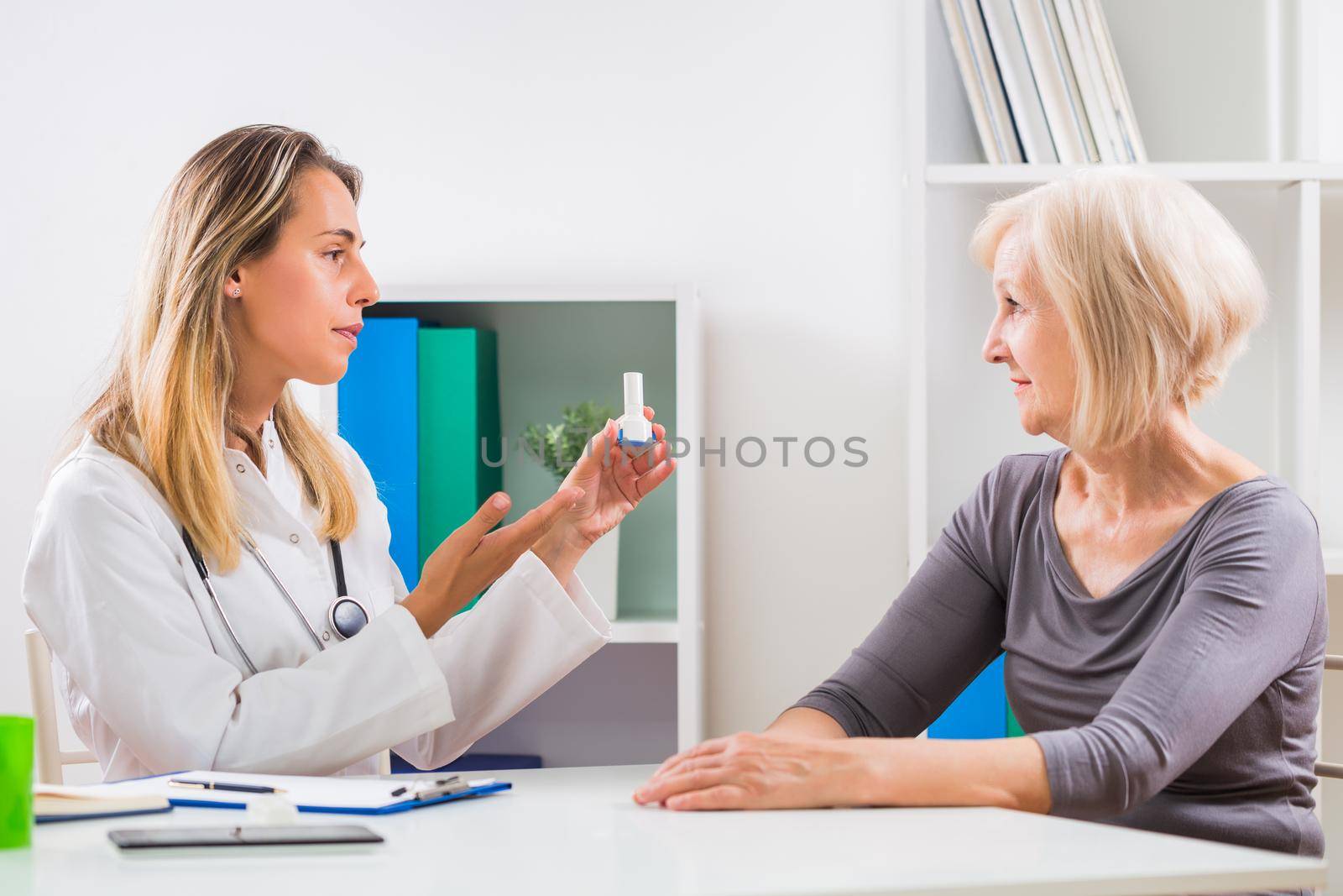 Female doctor is explaining how to use inhaler to her senior woman patient .