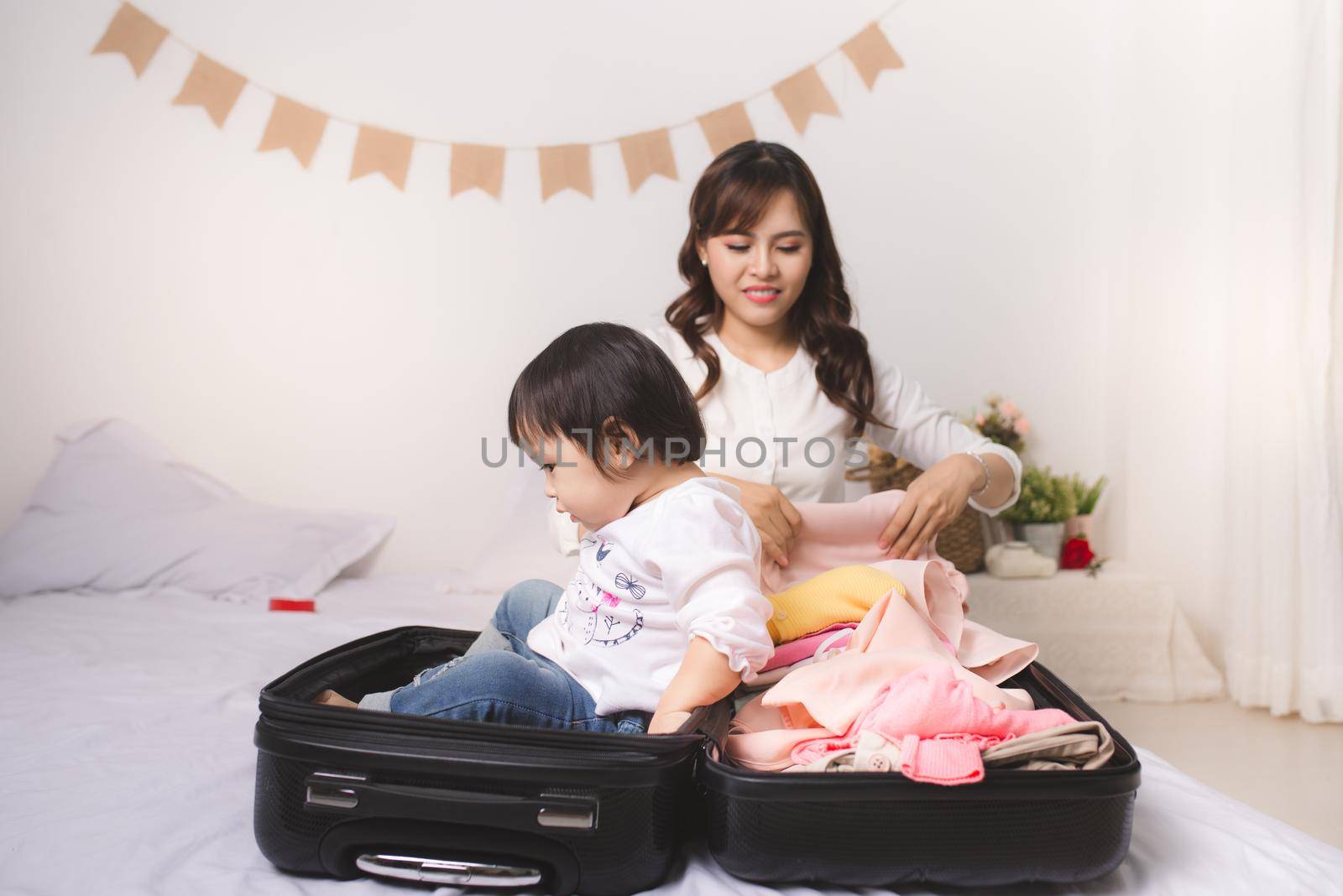 Asian mom and baby girl with suitcase baggage and clothes ready for traveling on vacation