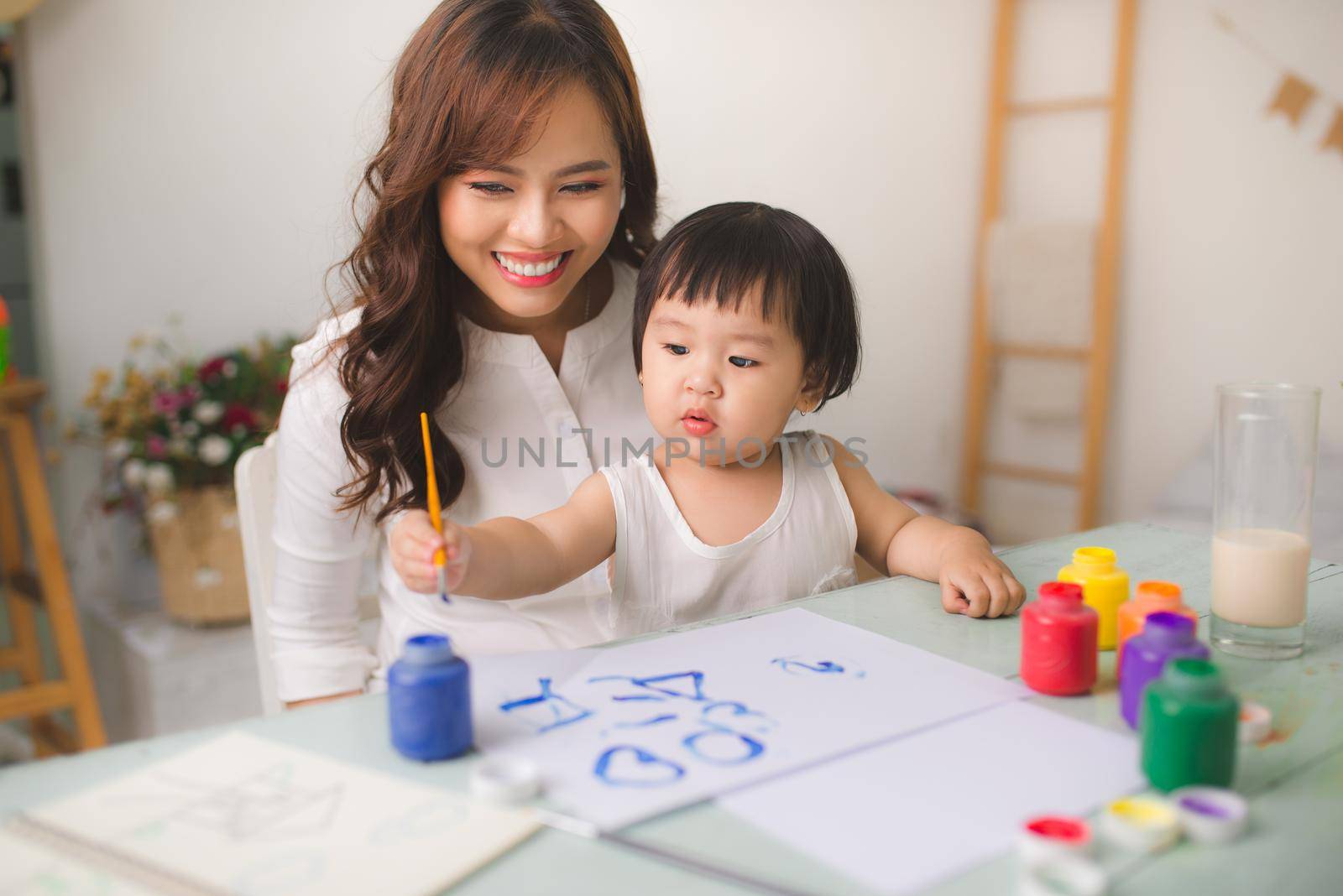 Happy family mother and daughter together paint. Asian woman helps her child girl. by makidotvn