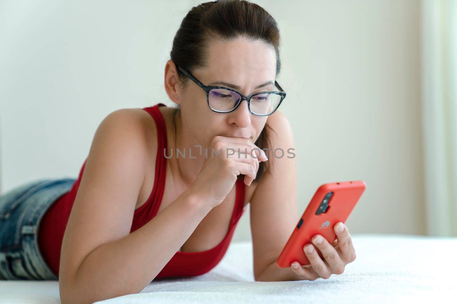 Woman talk via a smartphone video camera with look of trouble on her face while lying on bed.