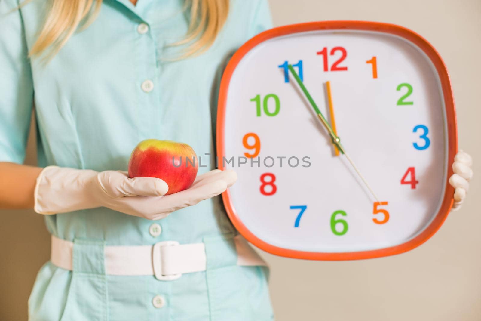 Image of medical nurse doctor holding apple and clock.Focus on apple.