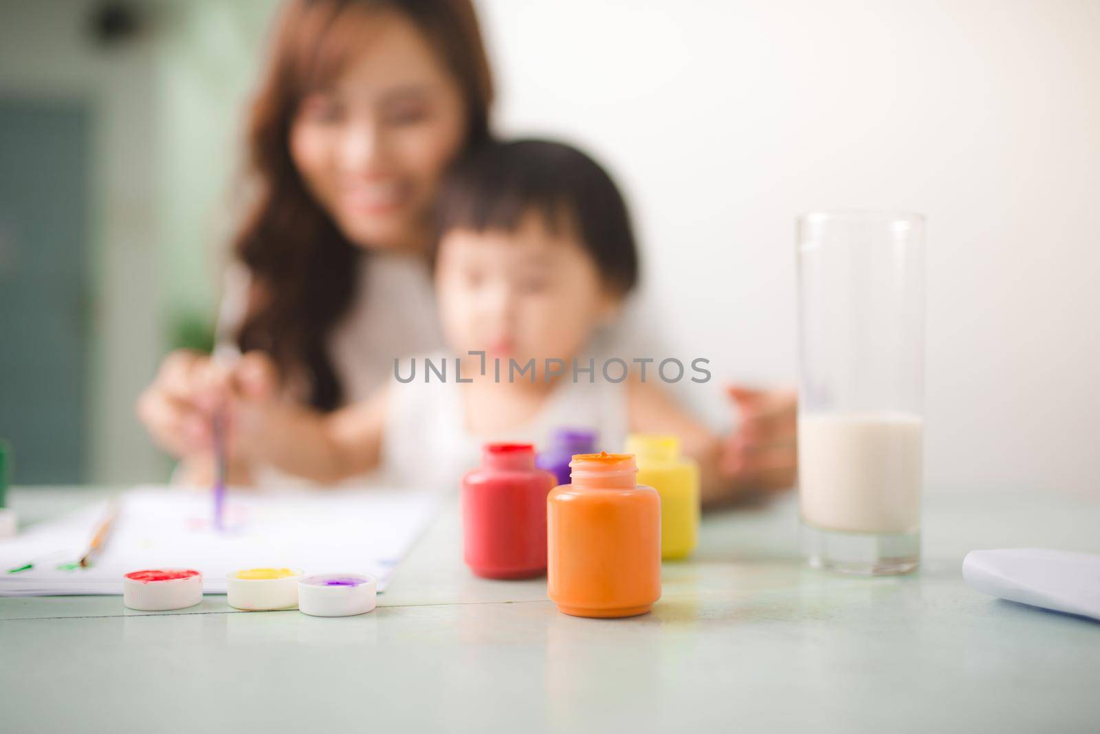 Happy family mother and daughter together paint. Asian woman helps her child girl.