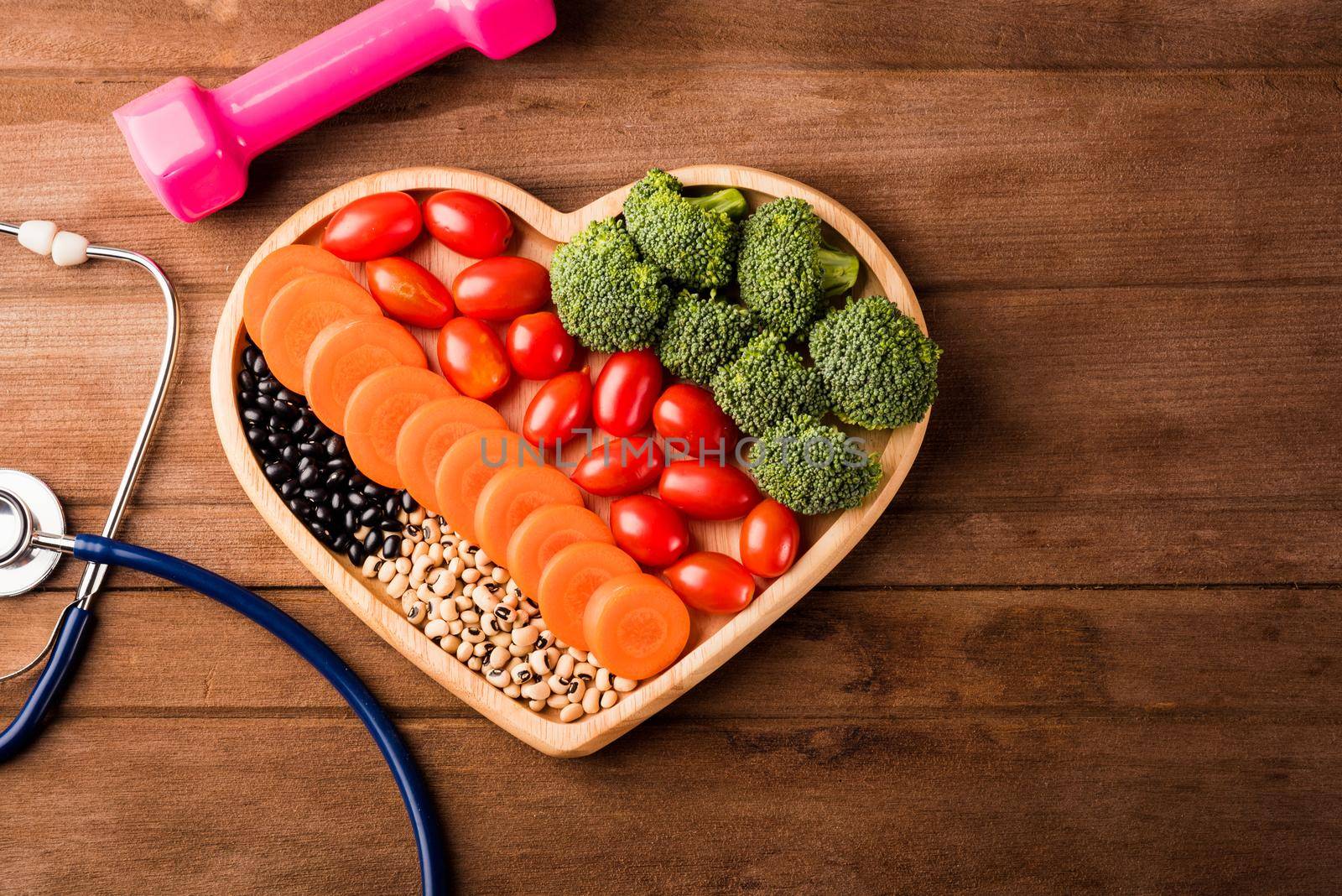 Top view of fresh organic fruits and vegetables in heart plate wood (carrot, Broccoli, tomato), doctor stethoscope and sport dumbbell on wooden table, Healthy lifestyle diet food concept