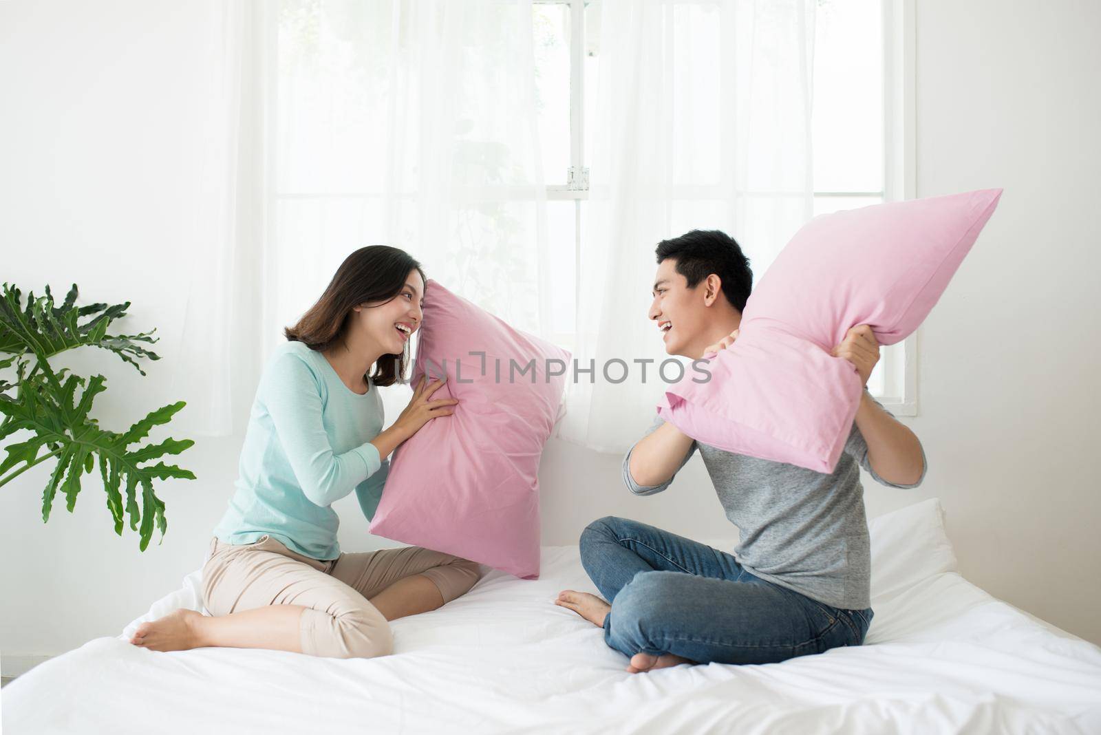 Happy asian couple having pillow fight in bed at home. Family fun concept. by makidotvn