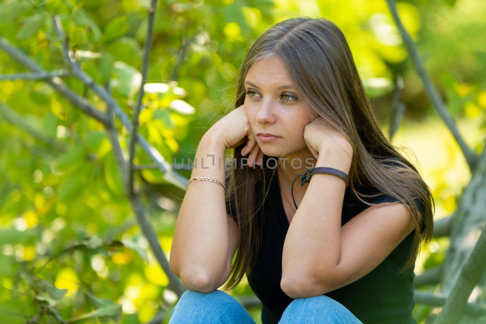 Sad girl sits on the background of foliage and sadly looks into the distance