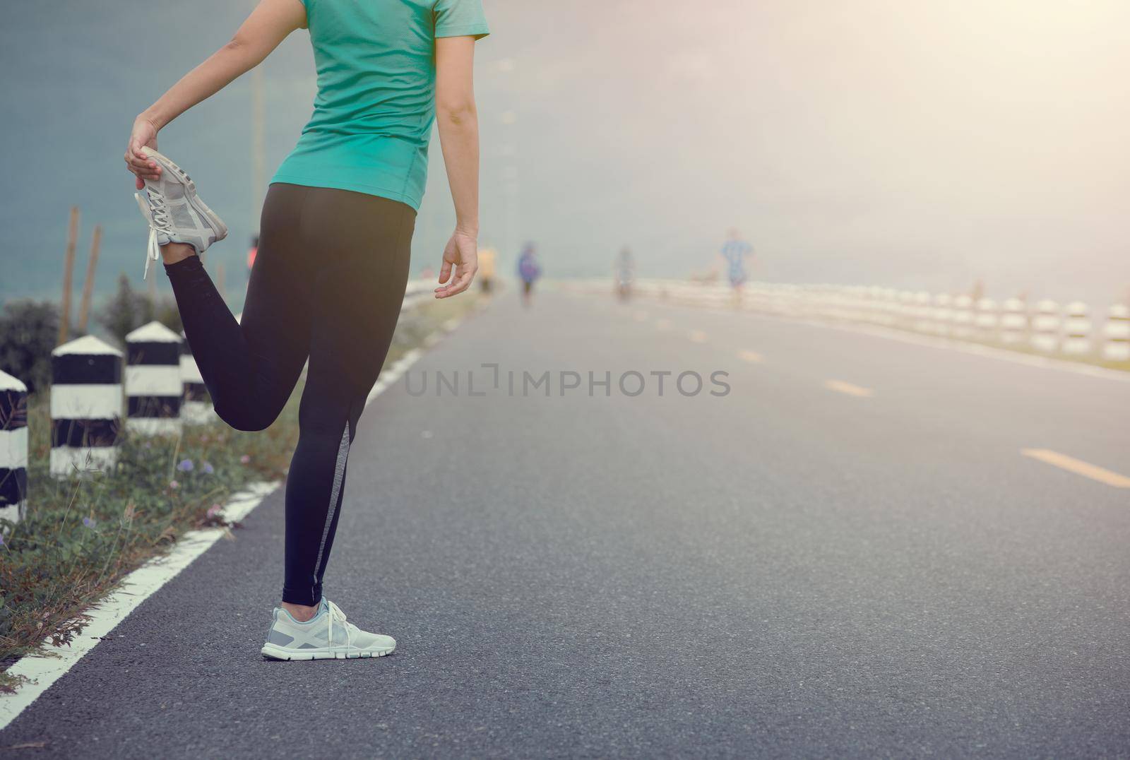 Young woman runner stretching legs before run on  road. by thanumporn