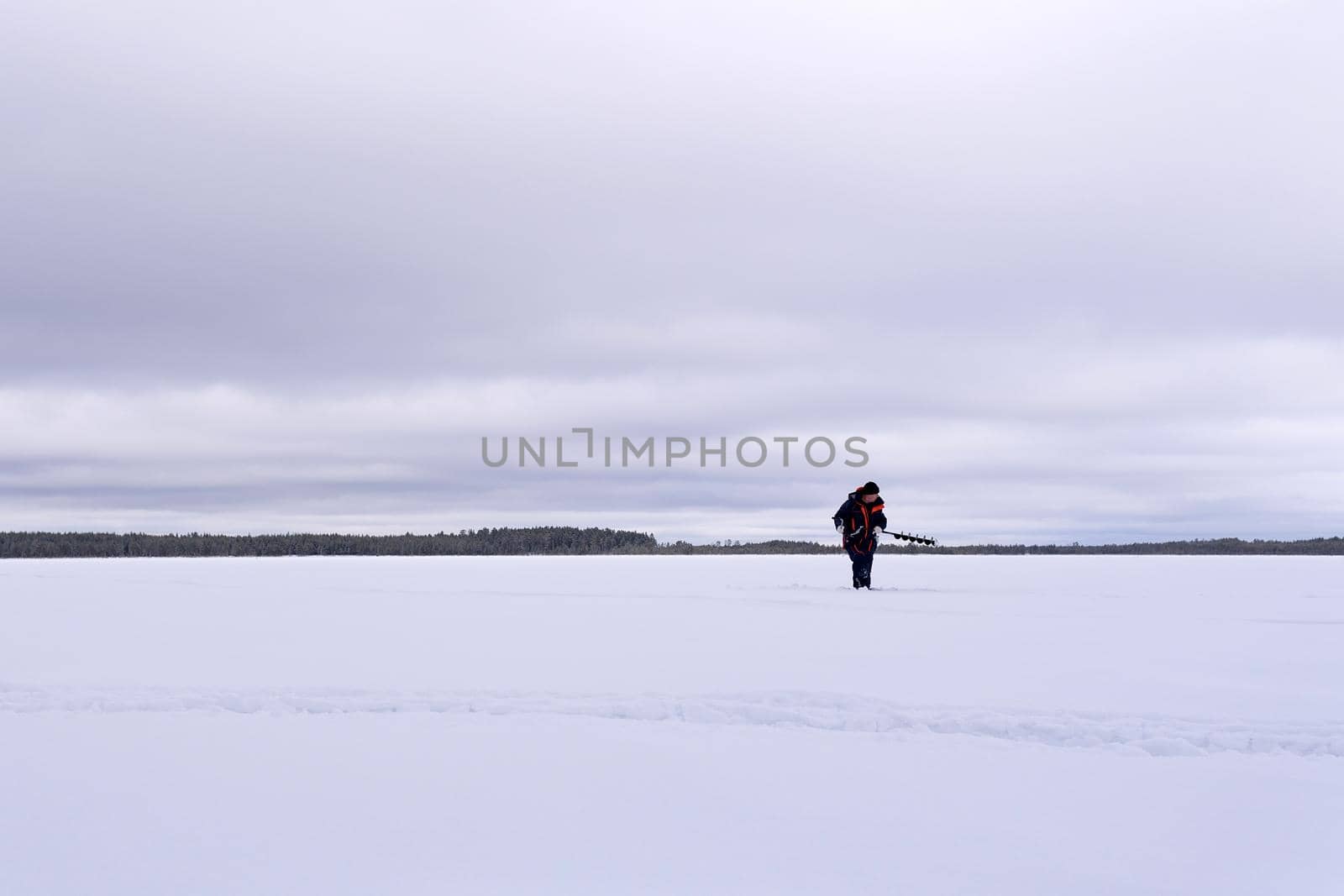 man drills holes for ice fishing with an electric auger. selective focus