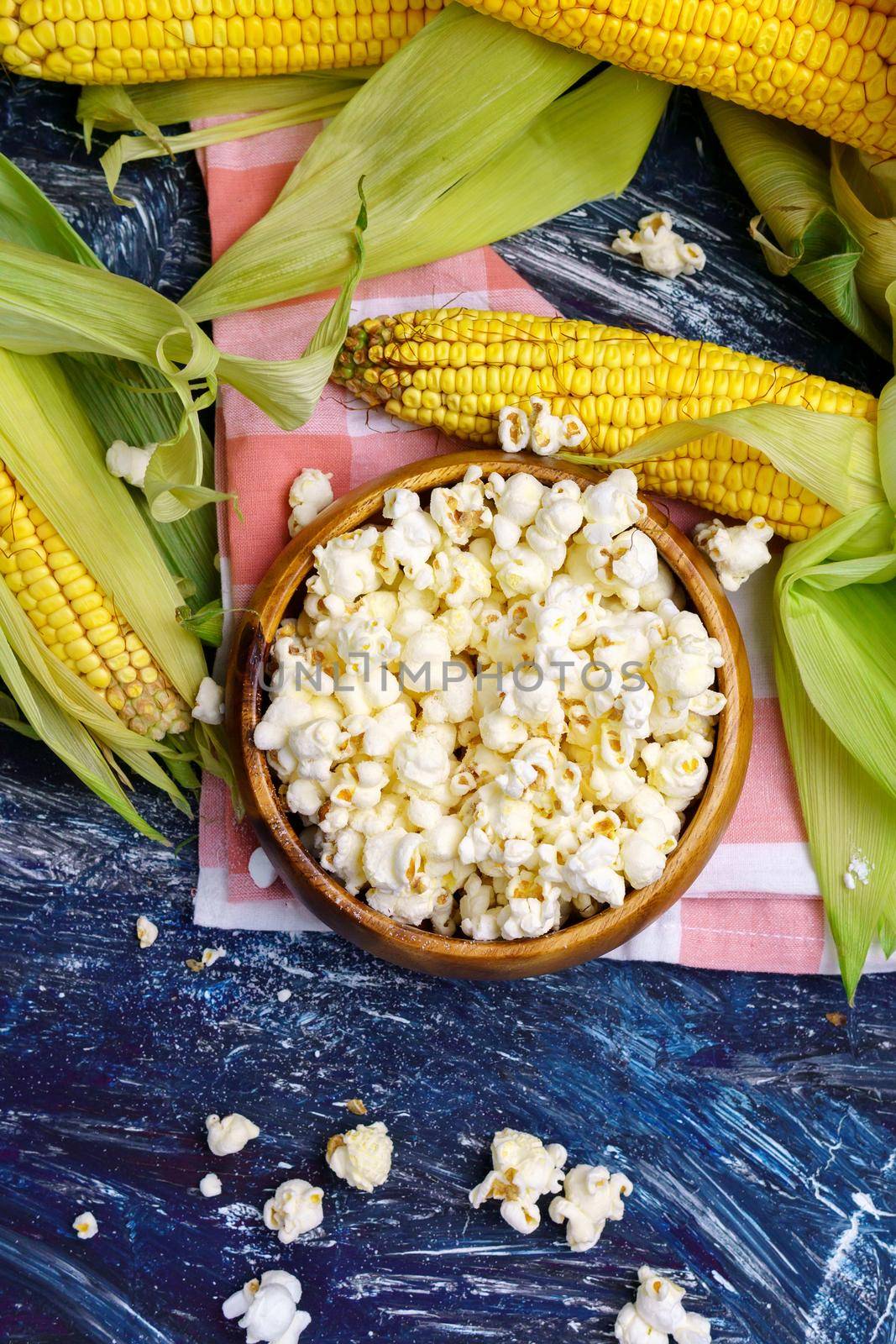 Tasty popcorn in a bowl on the table. Ears of fresh corn on a dark background. Vertical photo by darksoul72