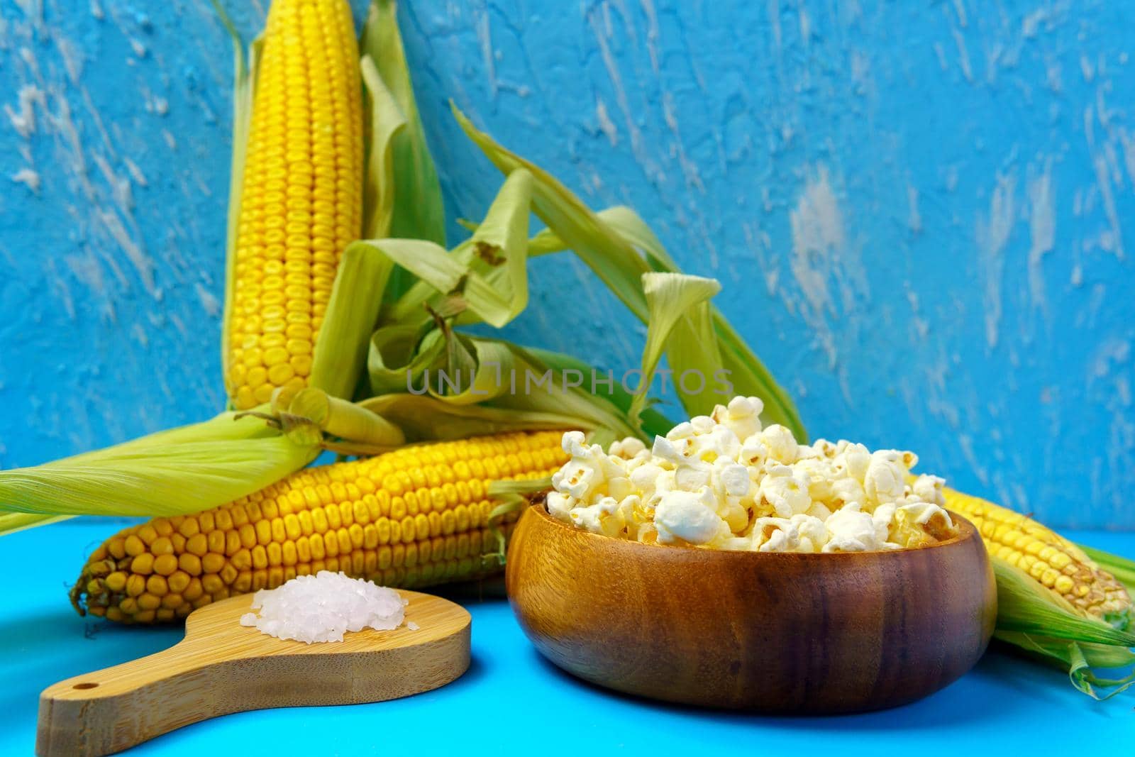 Corn on the cob, popcorn on a blue background. Topic - agro, corn cultivation, harvest.