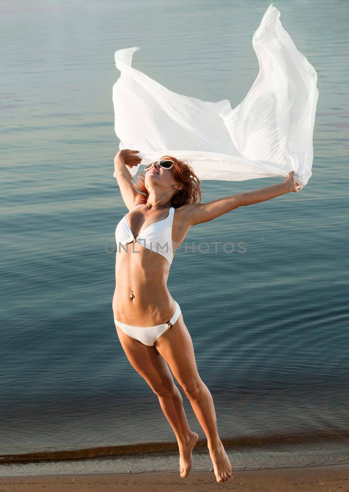 Slim girl in swimwear jumping with veil on a beach by nikitabuida