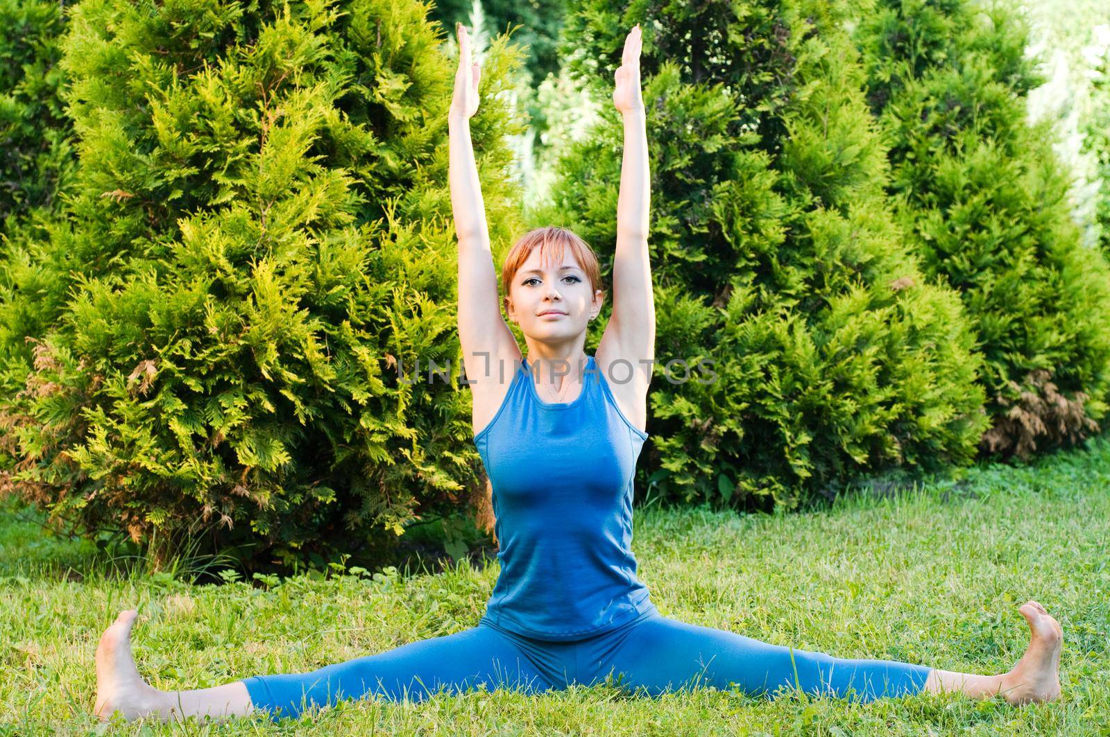Beautiful red woman doing fitness or yoga exercises outdoors in a green park