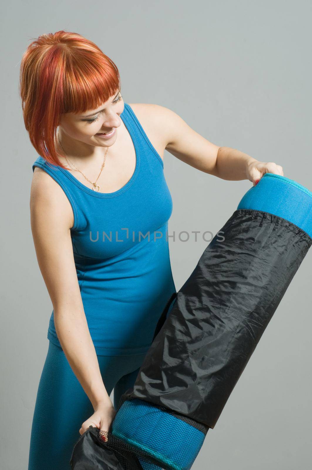 Red-haired fitness girl with yoga mat at the gym