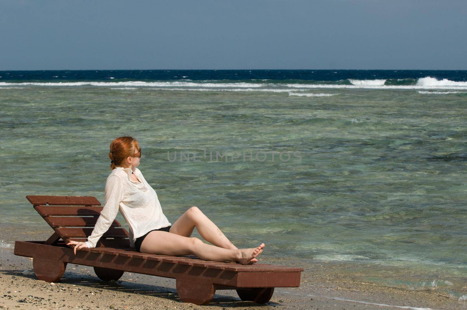 Beautiful red woman taking sun baths by the ocean