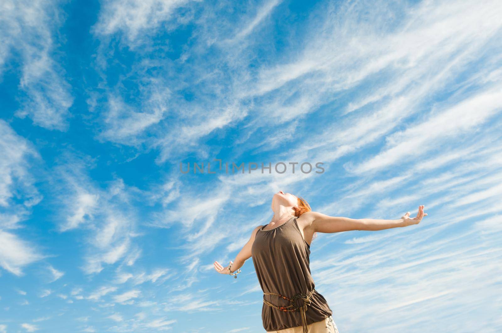 Beautiful young dancer performing yoga-dance outdoors with blue sky and clouds in the background