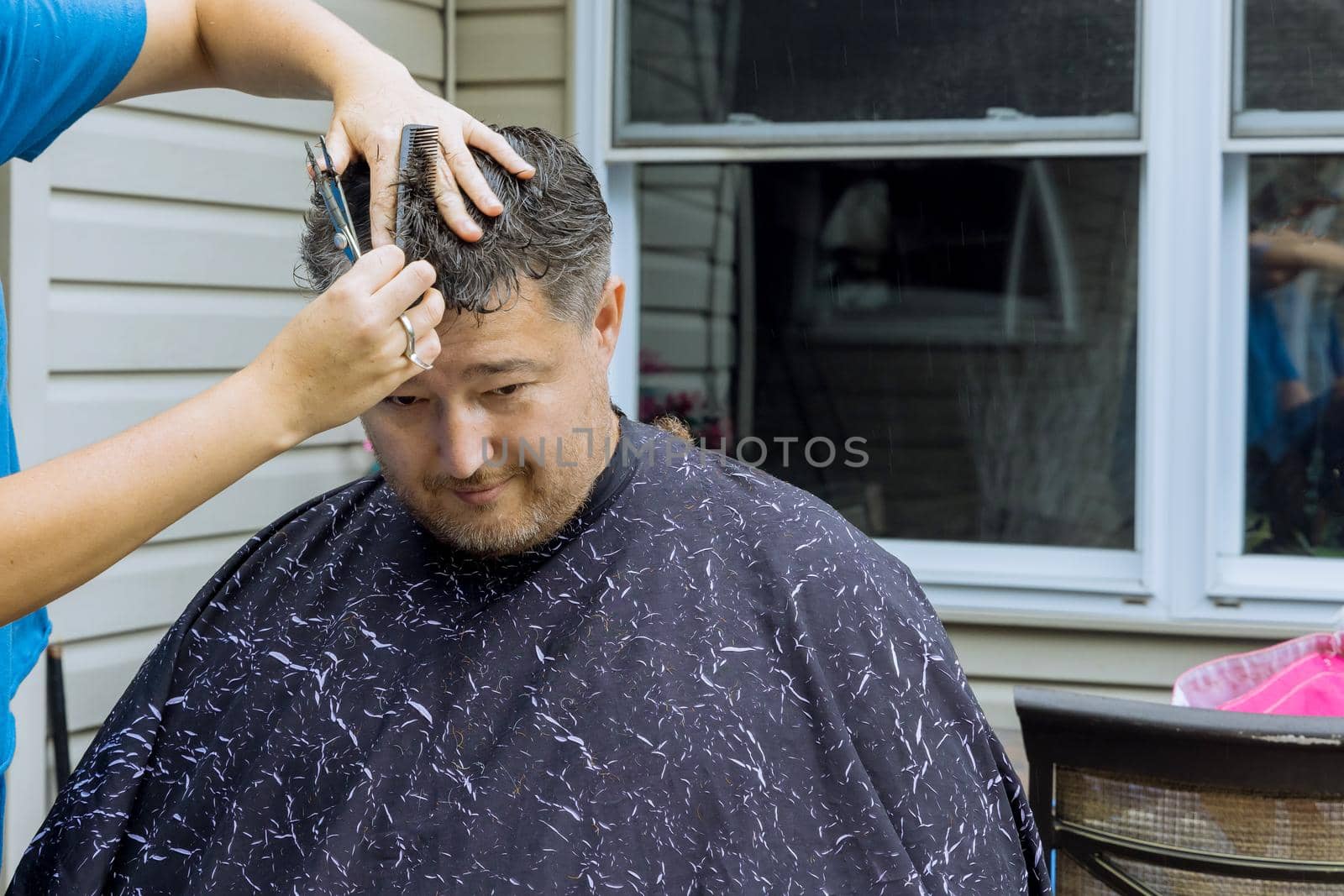 Professional barber with man getting haircut while sitting in chair at home outside