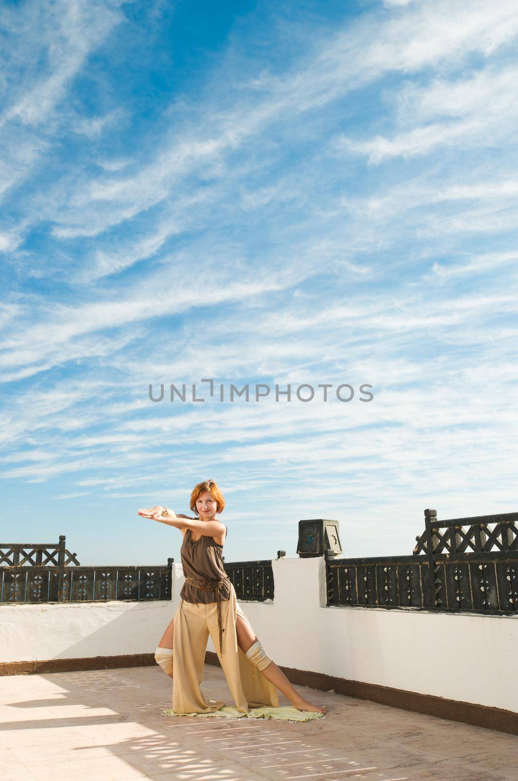 Beautiful young dancer performing yoga-dance outdoors with blue sky and clouds in the background