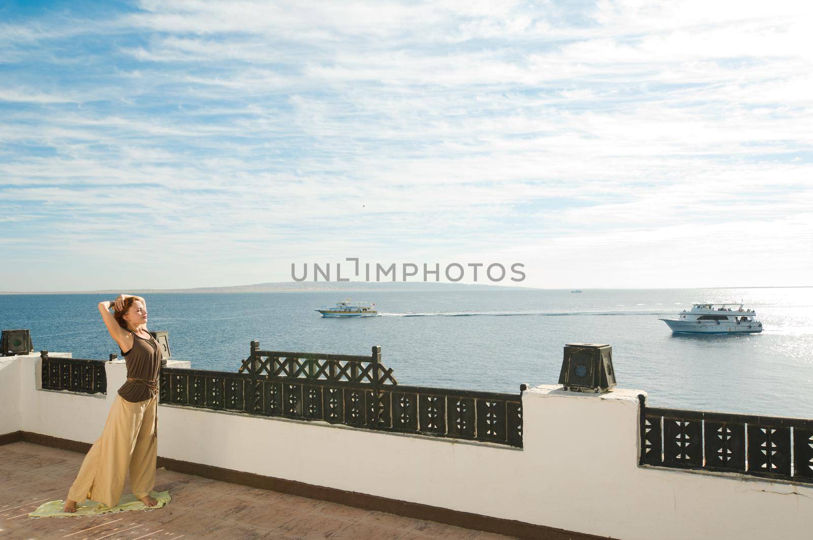 Beautiful young dancer performing yoga-dance outdoors with blue sky and clouds in the background