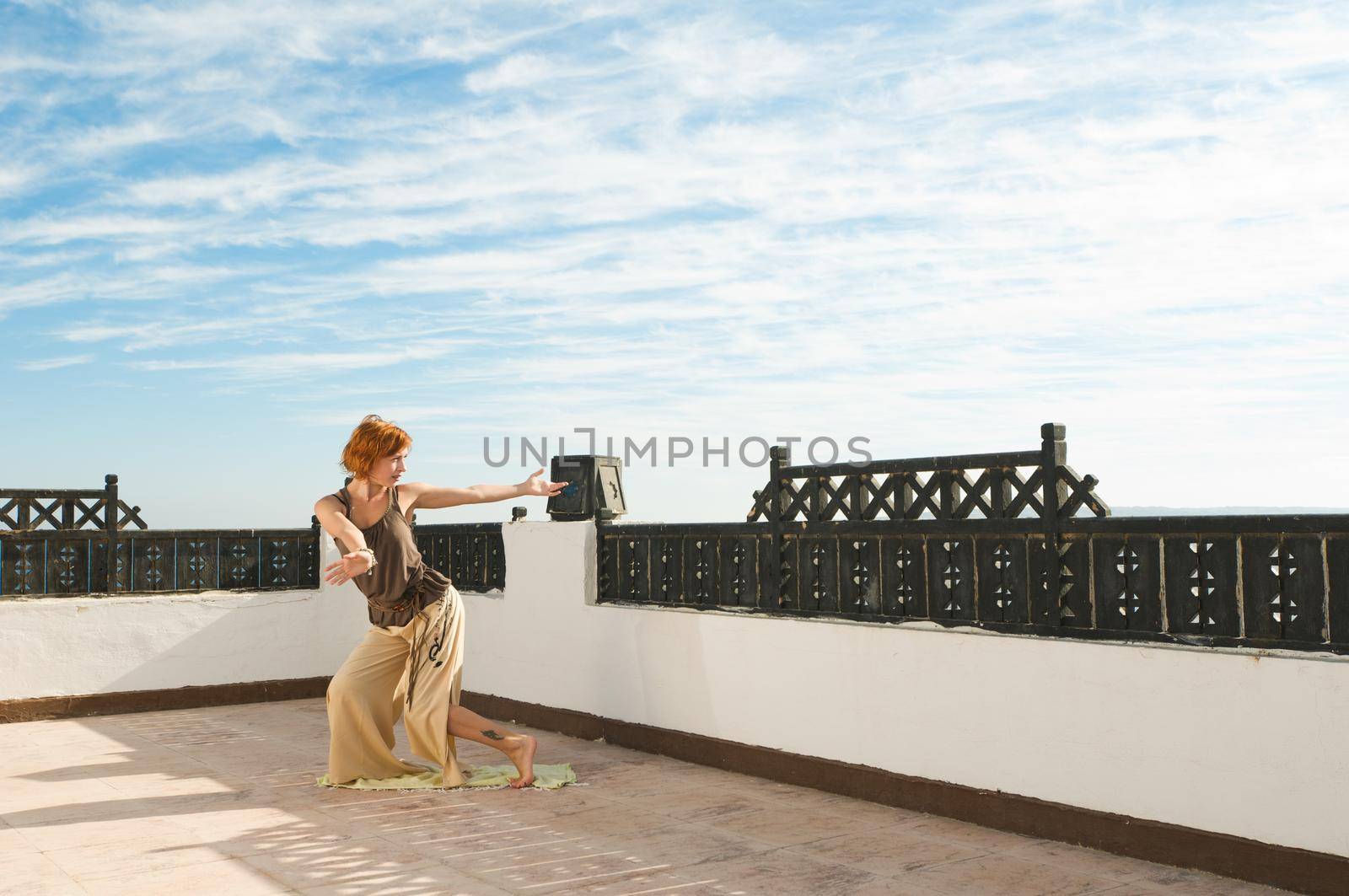 Beautiful young dancer performing yoga-dance outdoors with blue sky and clouds in the background