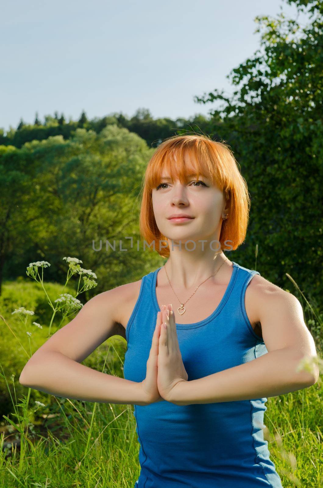 Beautiful red haired woman practicing fitness yoga outdoors on a summer day