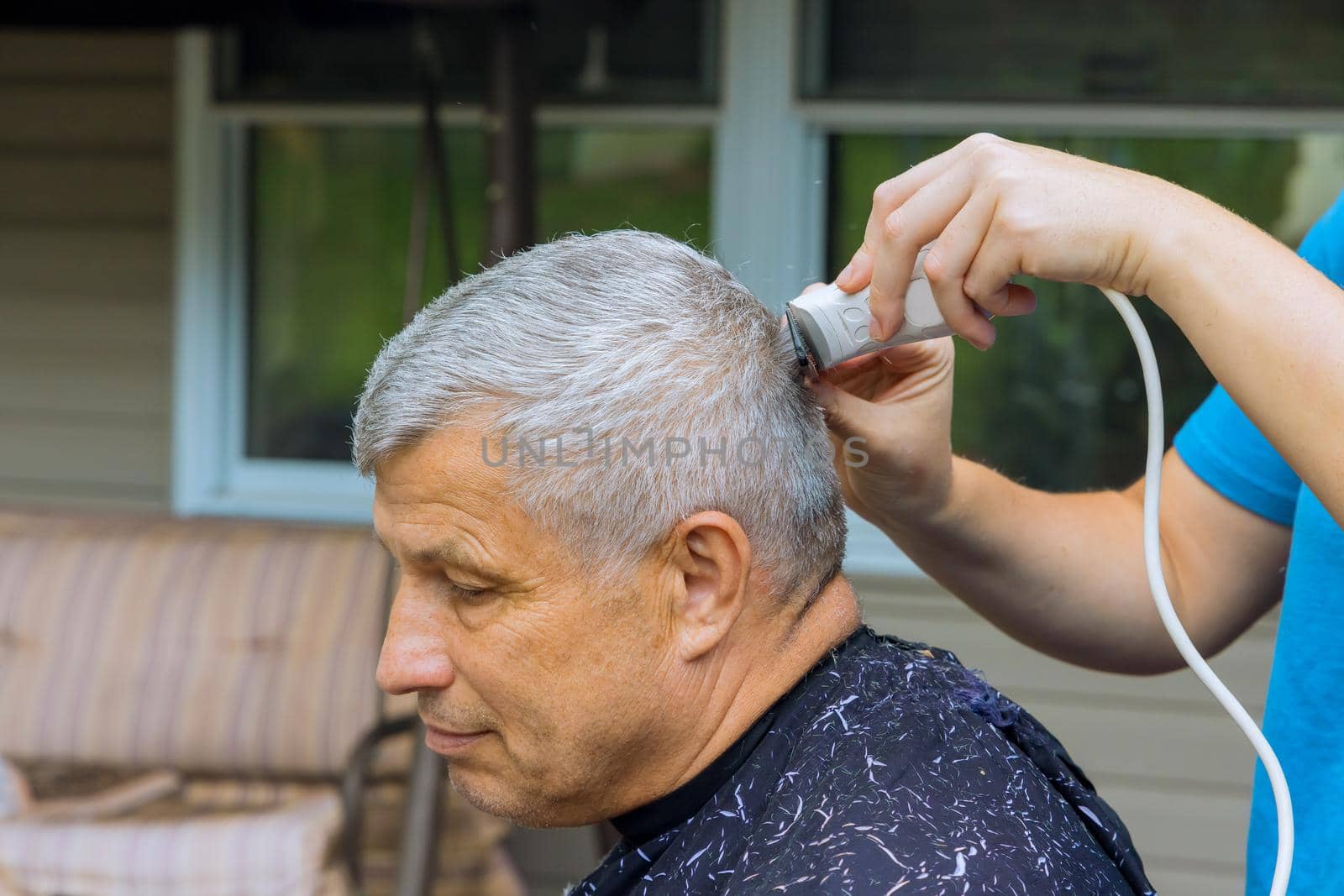 Professional barber with man getting haircut while sitting in chair at home by ungvar