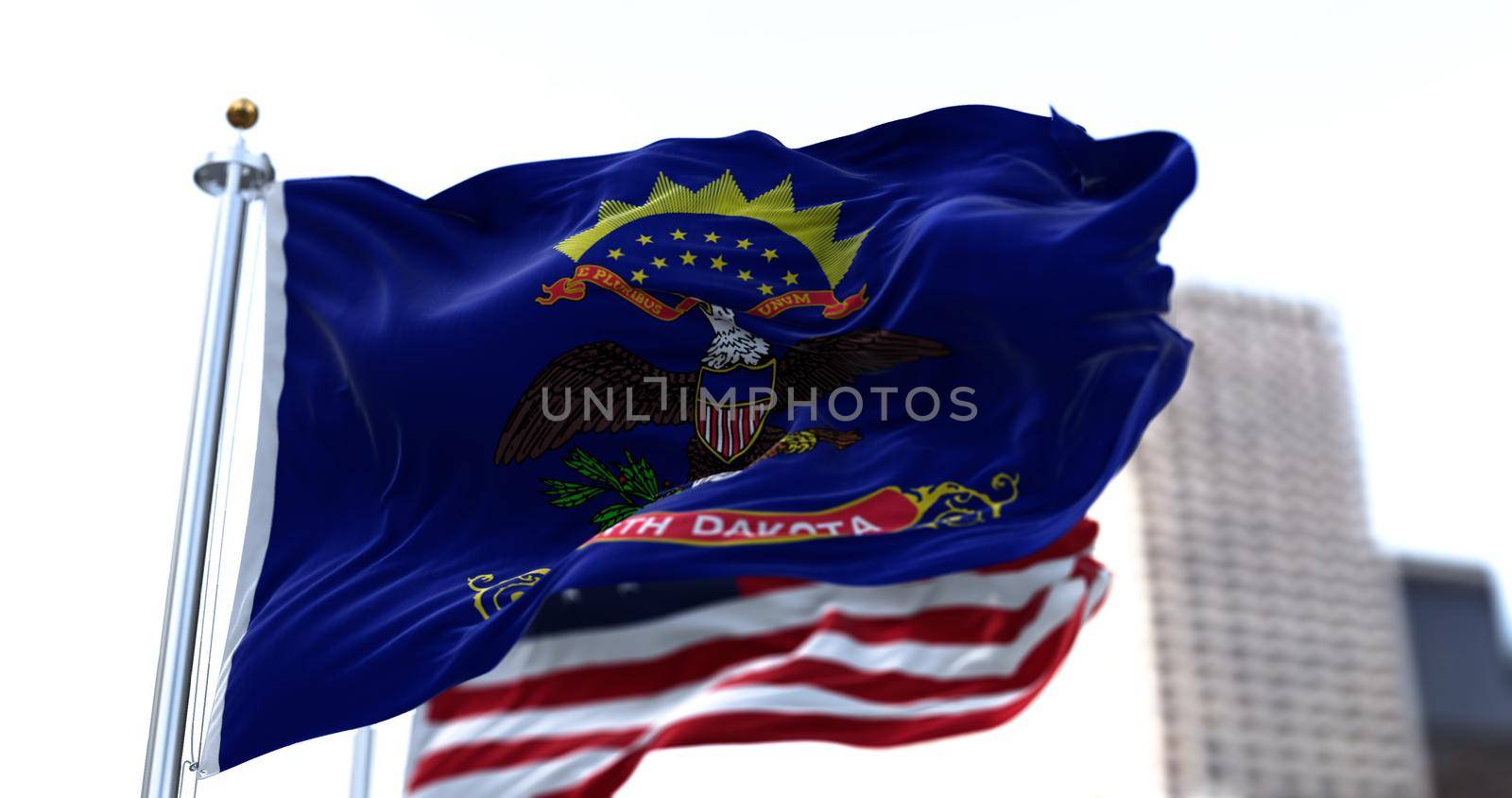 the flag of the US state of North Dakota waving in the wind with the American stars and stripes flag blurred in the background. North Dakota was it admitted in 1889 as the 39th of the Union. Independence and unity