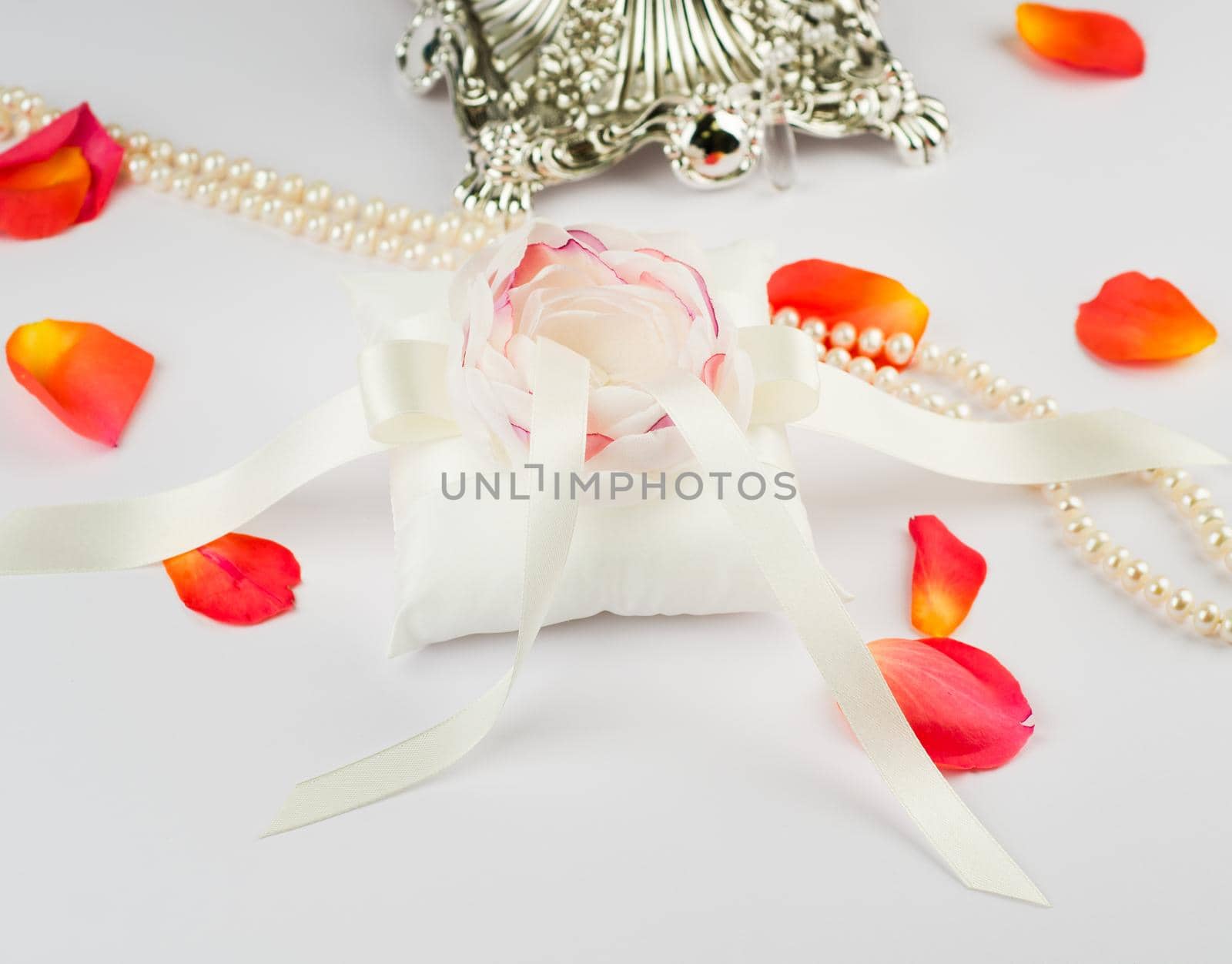 Exquisite pillow for wedding rings on gray background with rose petals