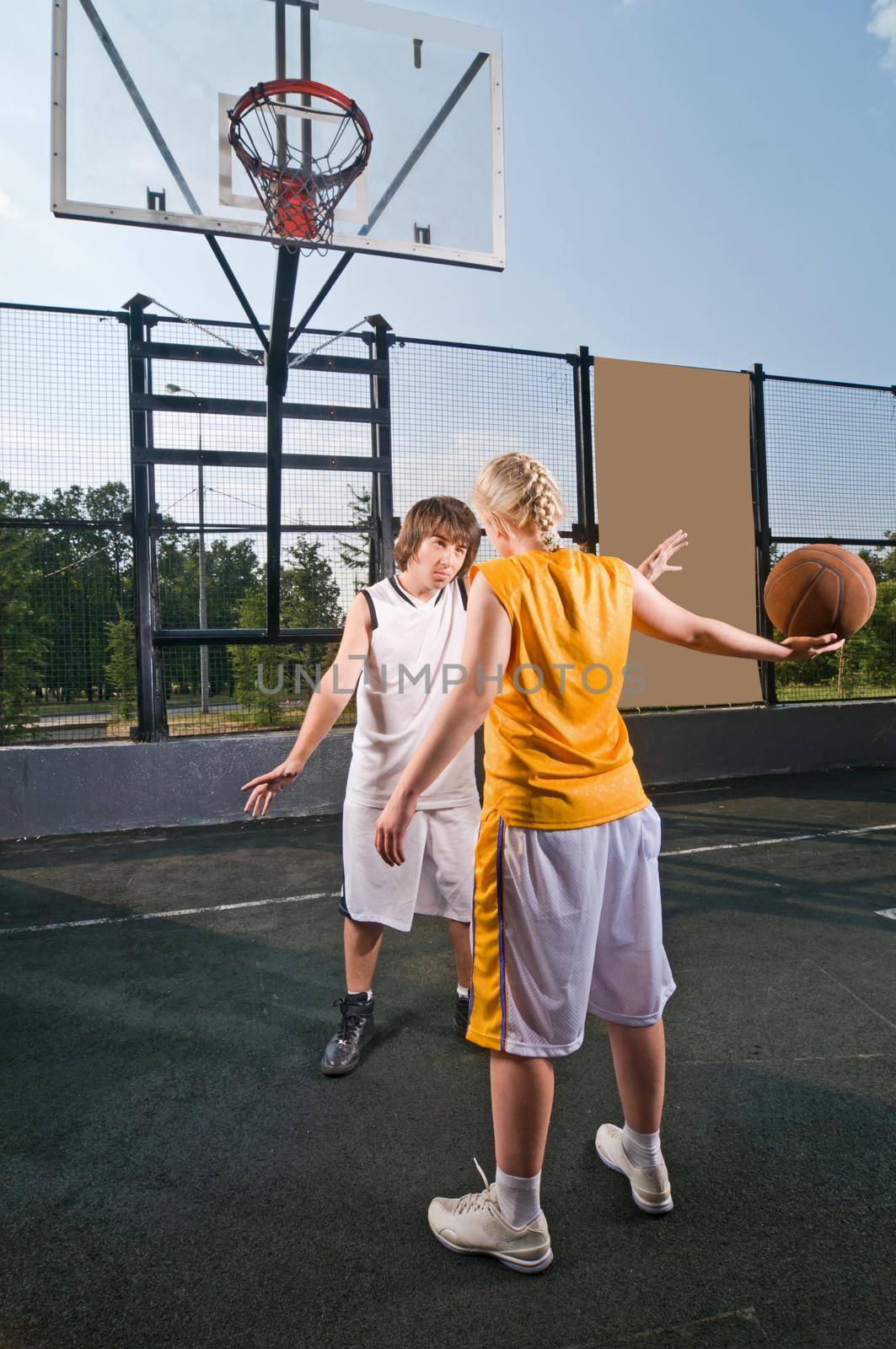 Two teenagers playing streetball with boy defending against girl