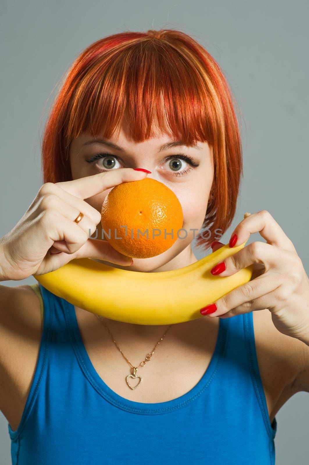 Red-haired girl with banana and orange in her hands. Focus is on the fruits forming a smiley :)